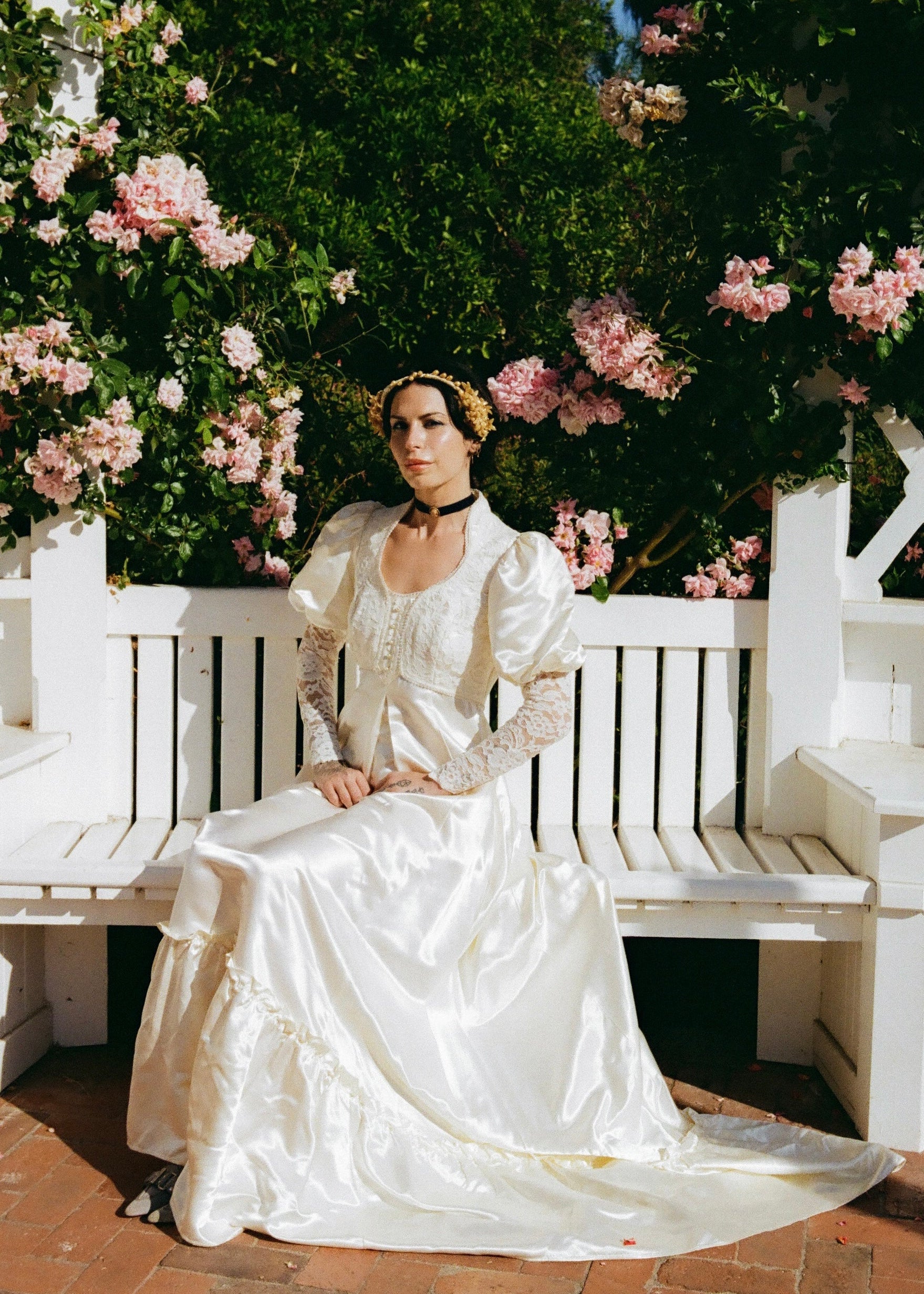 Woman in a white vintage dress sitting on a white bench with pink flowers in the background