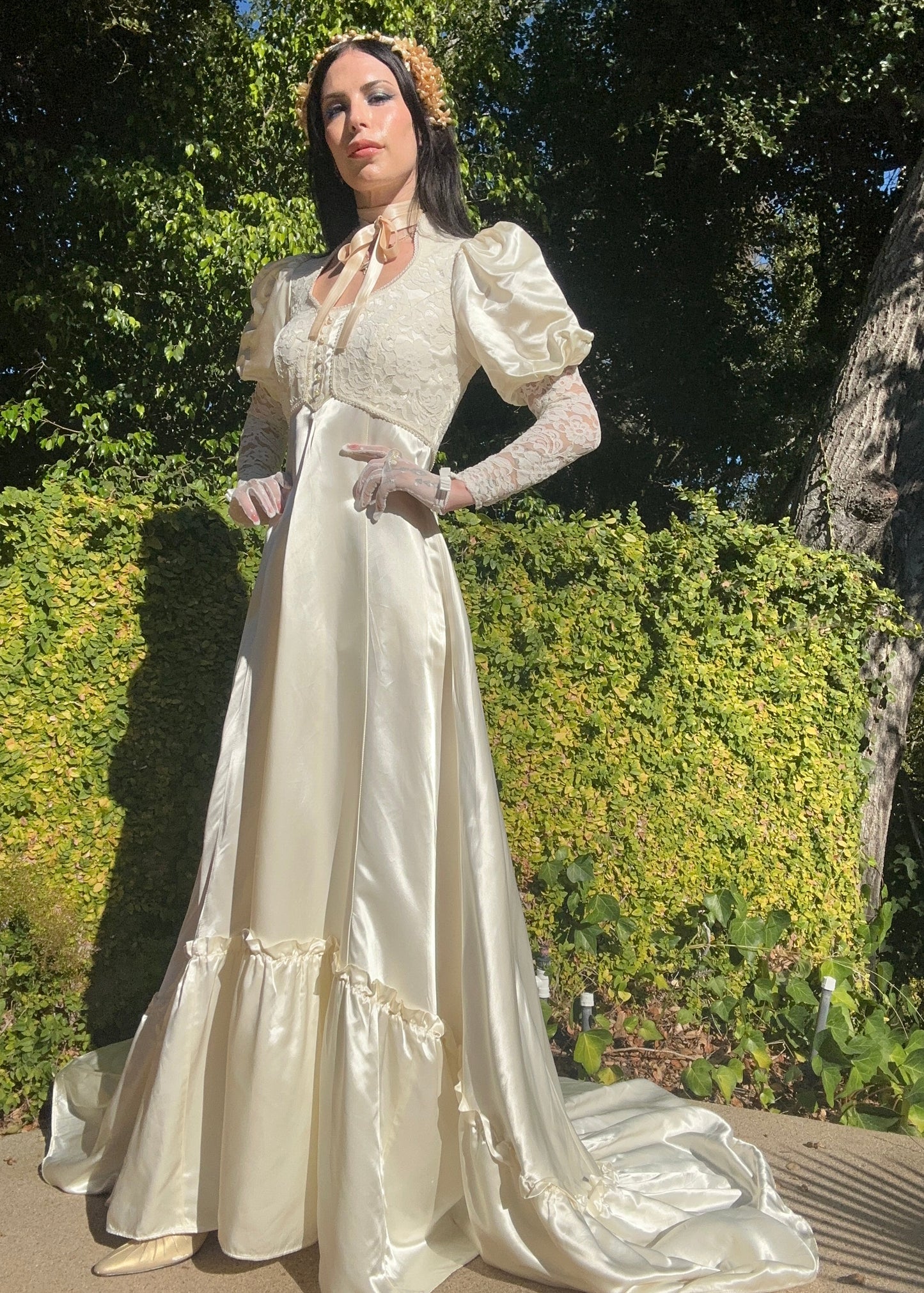 Person in a white vintage-style dress standing outdoors with greenery in the background