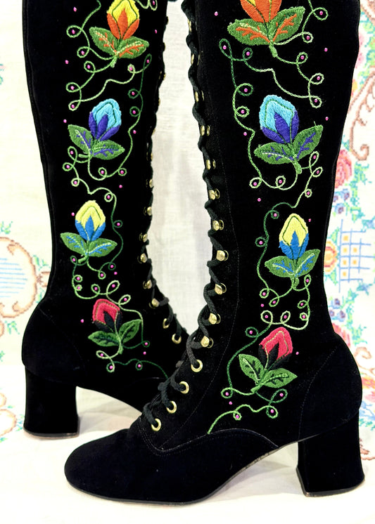 Black knee-high 1960's suede penny lane gogo boots with colorful floral embroidery on a decorative background