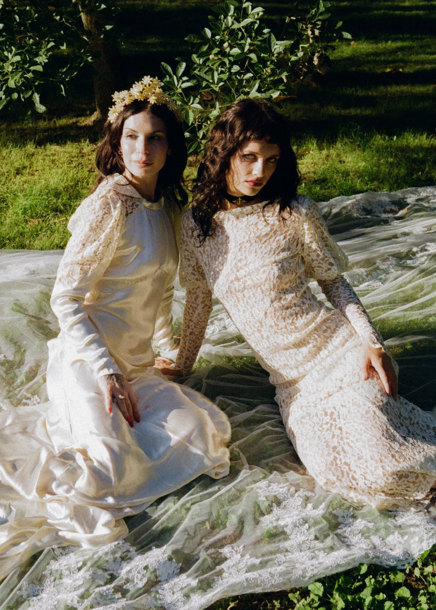 Two women wearing antique lace wedding dresses sitting in a grassy field