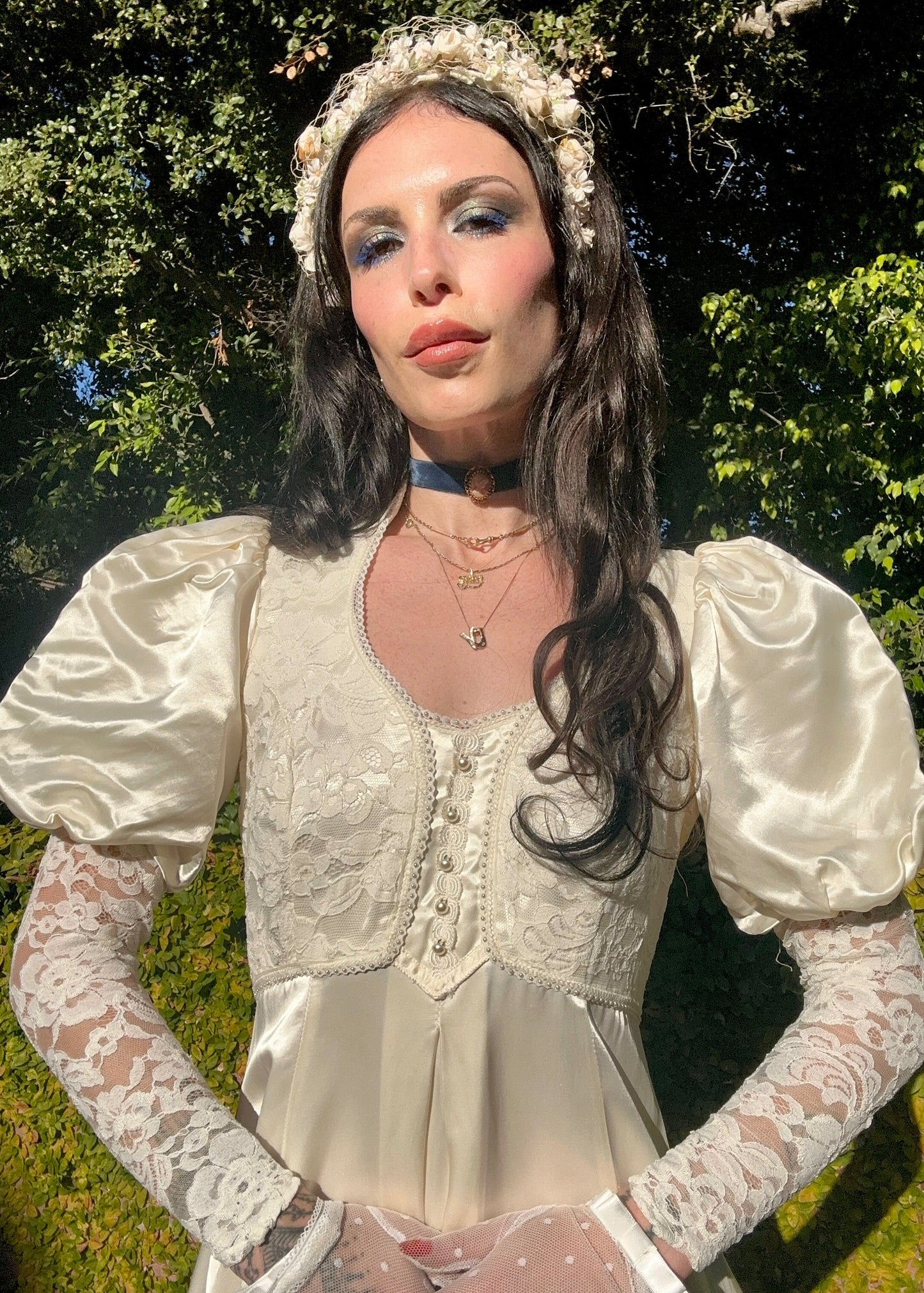 Woman in a vintage-style dress with lace sleeves and a headpiece outdoors.