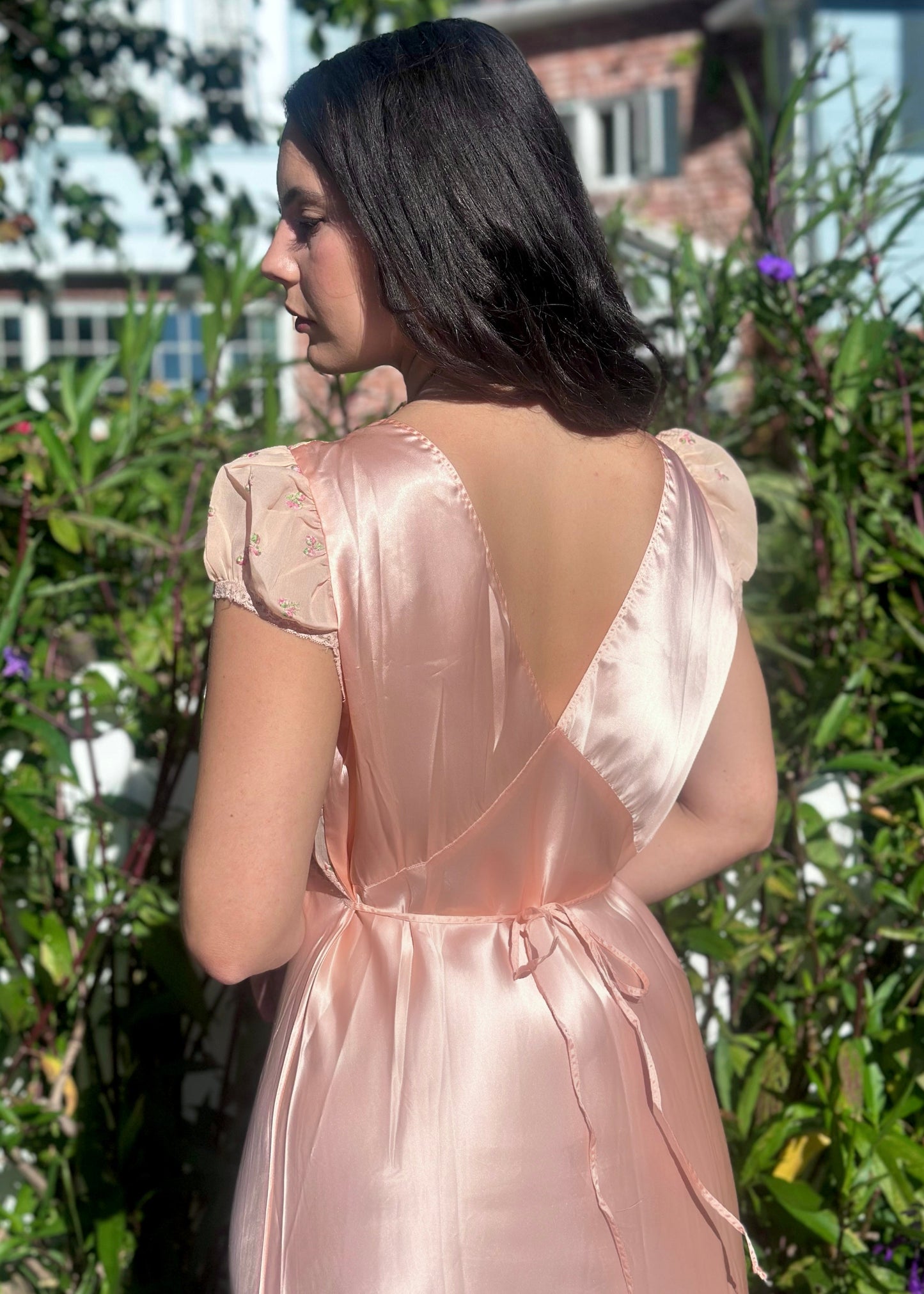 Woman wearing an sntiwue pink satin dress standing outdoors with greenery in the background
