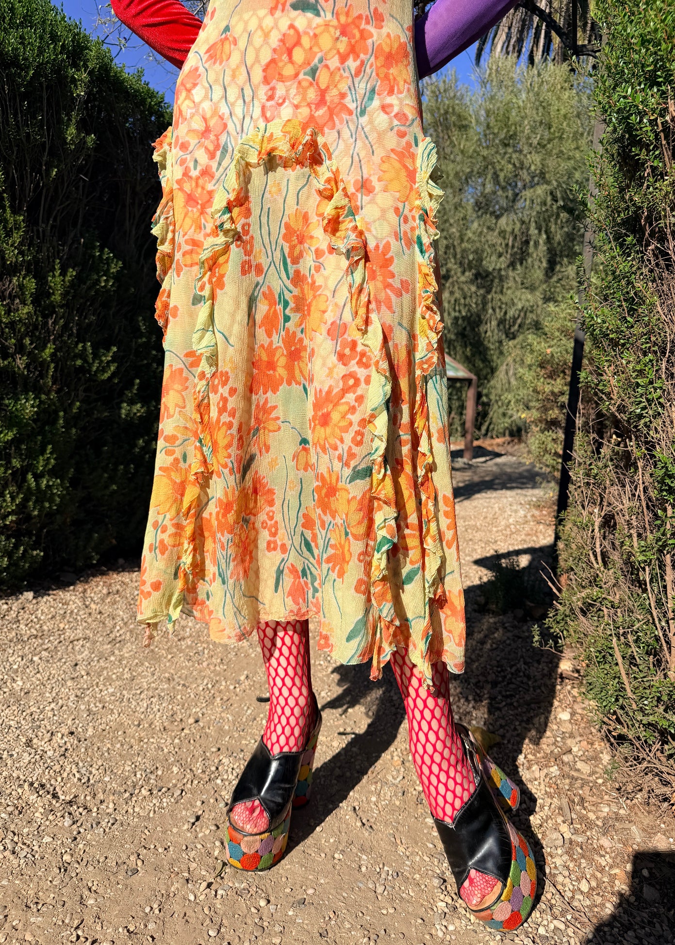 Person wearing a colorful floral dress with patterned leggings and platform shoes outdoors.