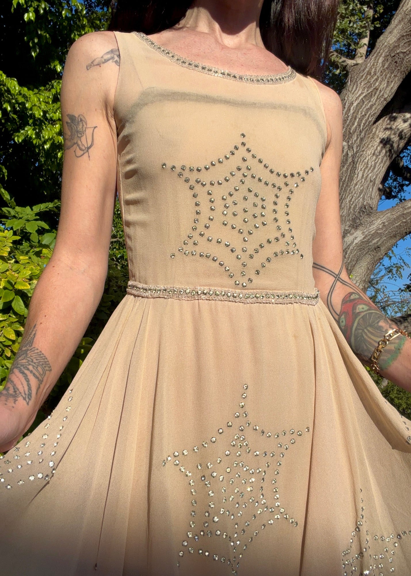 Beige antique 1920's silk chiffon dress with star or spider web design embellishments made from rhinestones worn by a person outdoors.