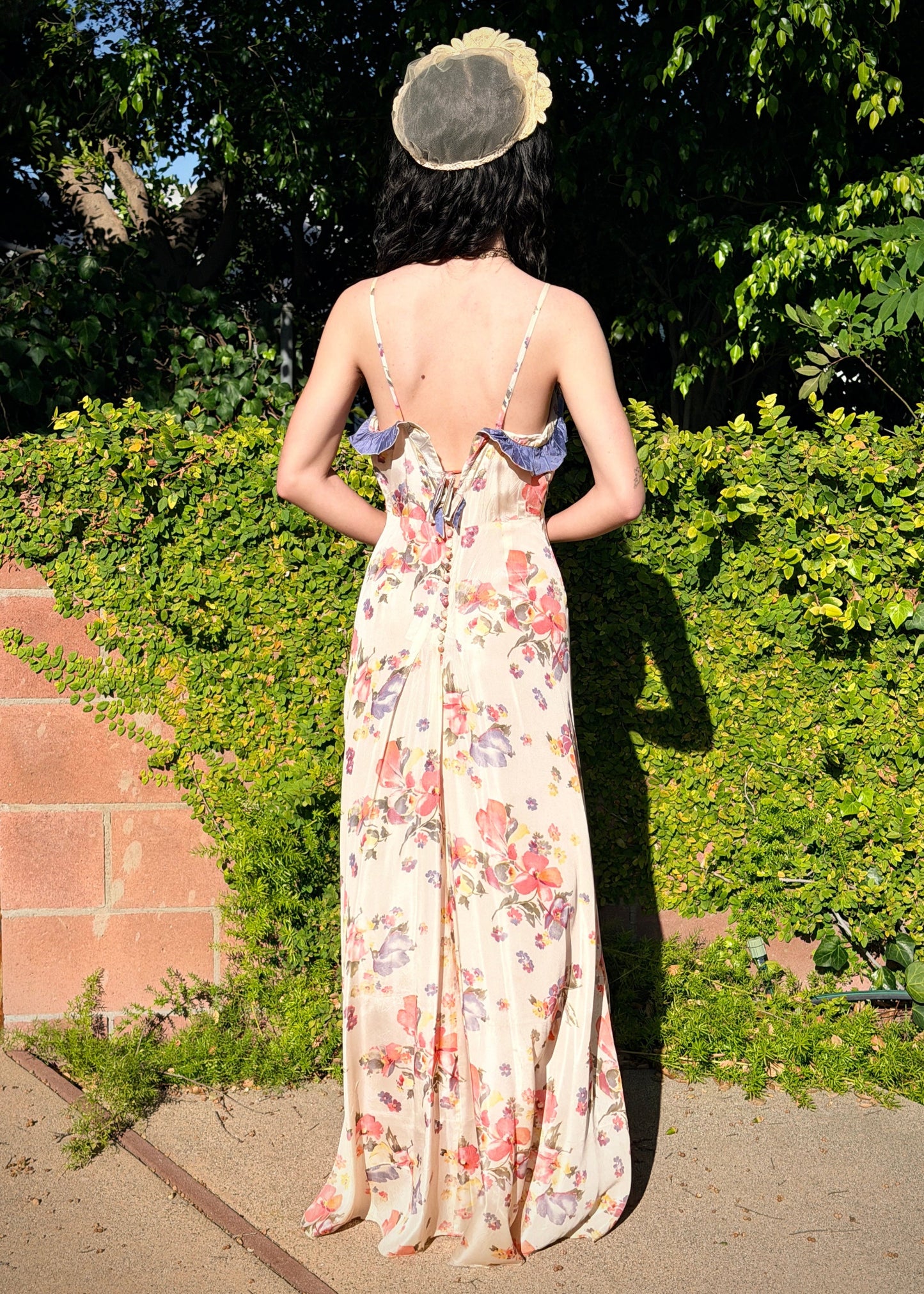 Woman in an antique 1930's floral dress with a headpiece standing outdoors with greenery in the background