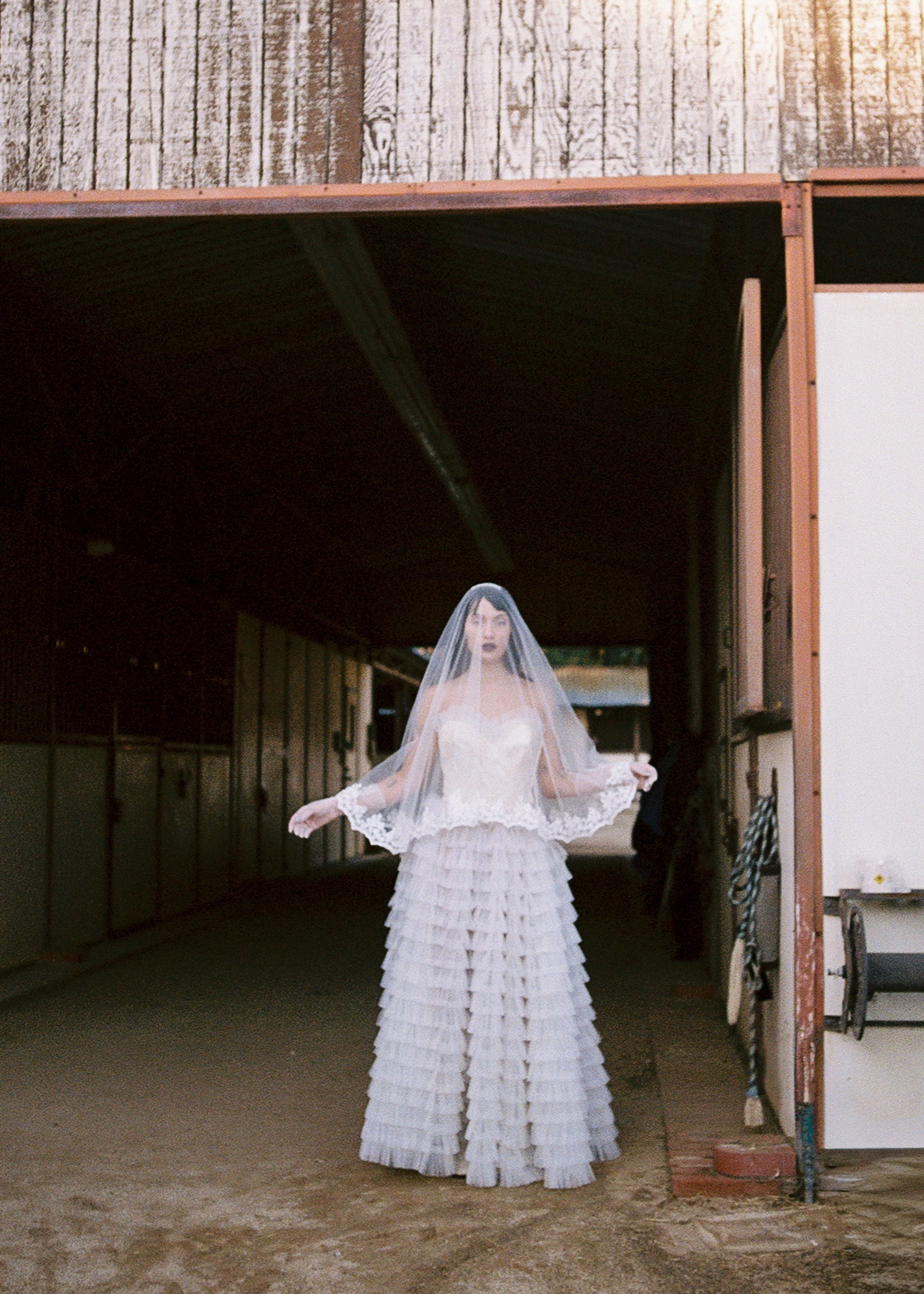 Woman in a white wedding dress standing in front of a rustic building.