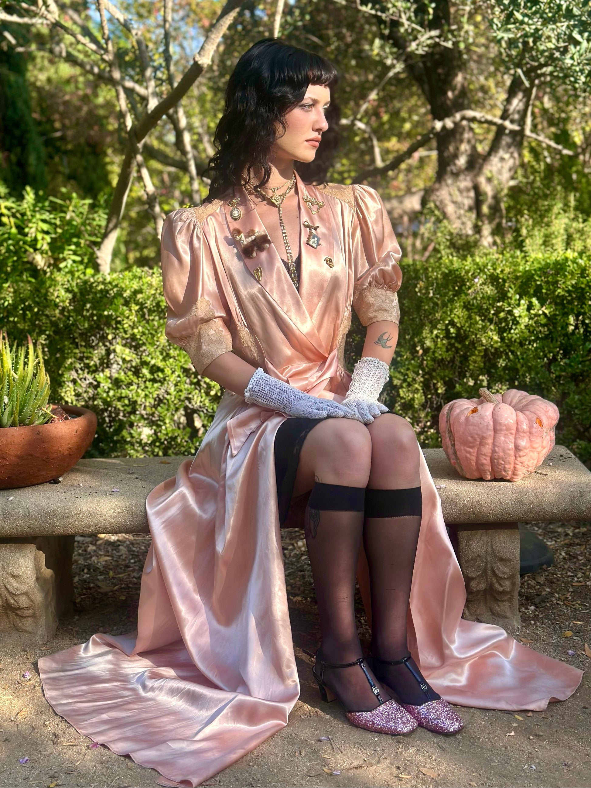 Woman in a vintage-style dress sitting on a stone bench in a garden.