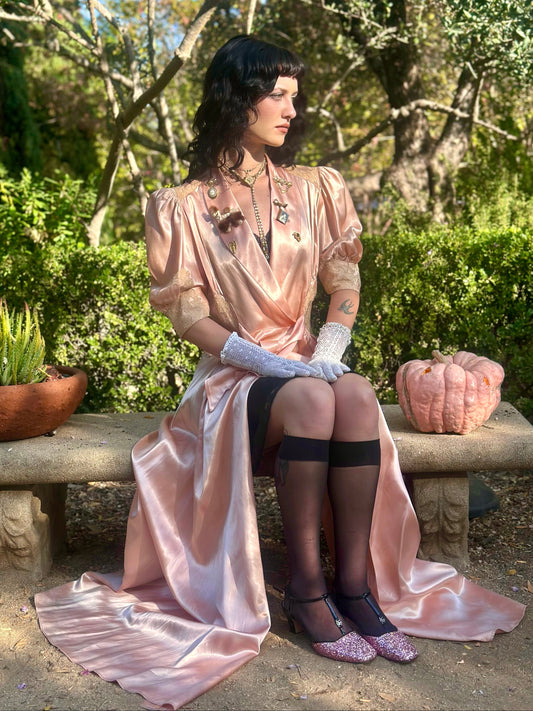 Woman in a vintage-style dress sitting on a stone bench in a garden.