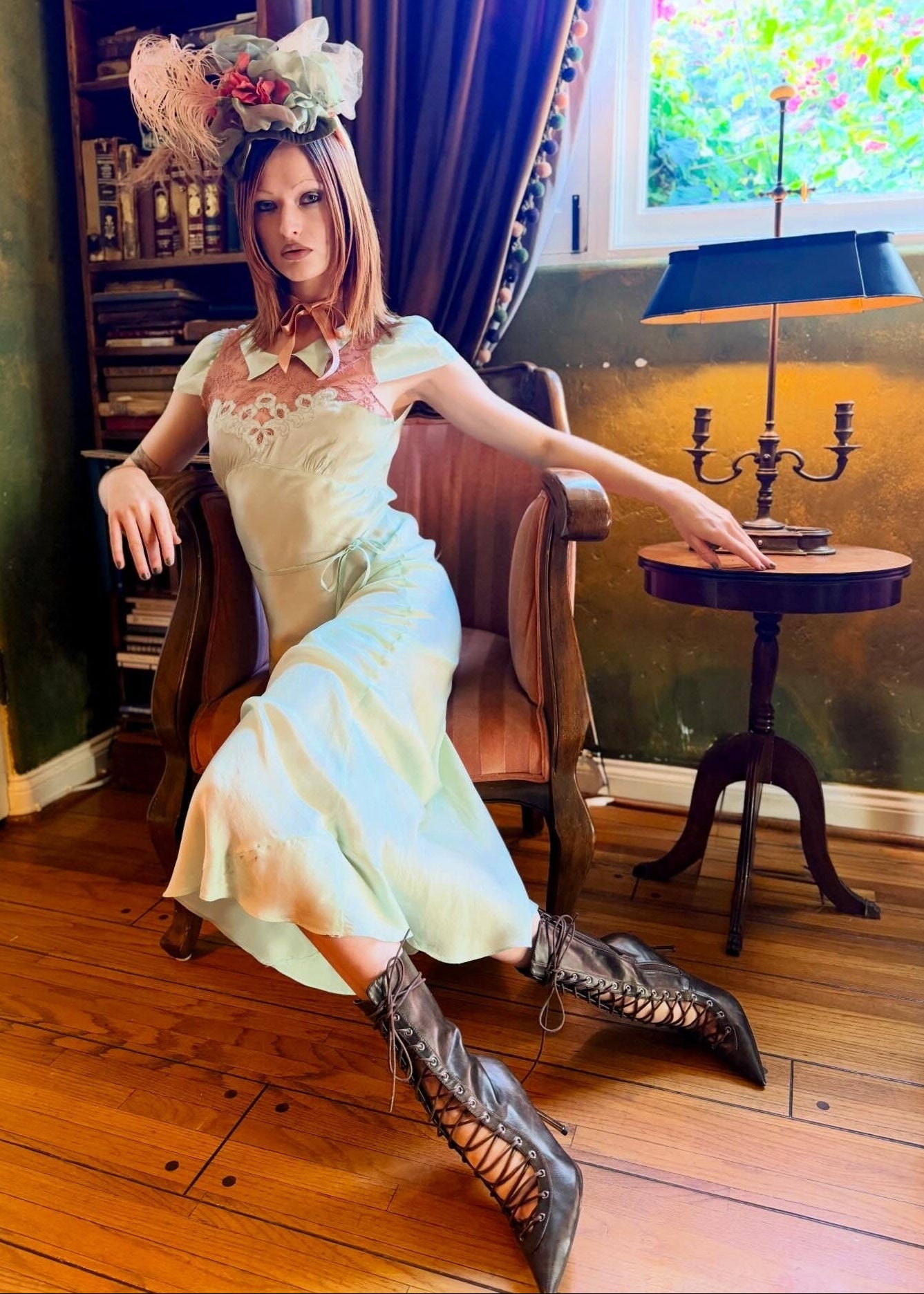 Woman in an antique 1930's silk slip in mint green with a floral headpiece against a wall with framed paintings.