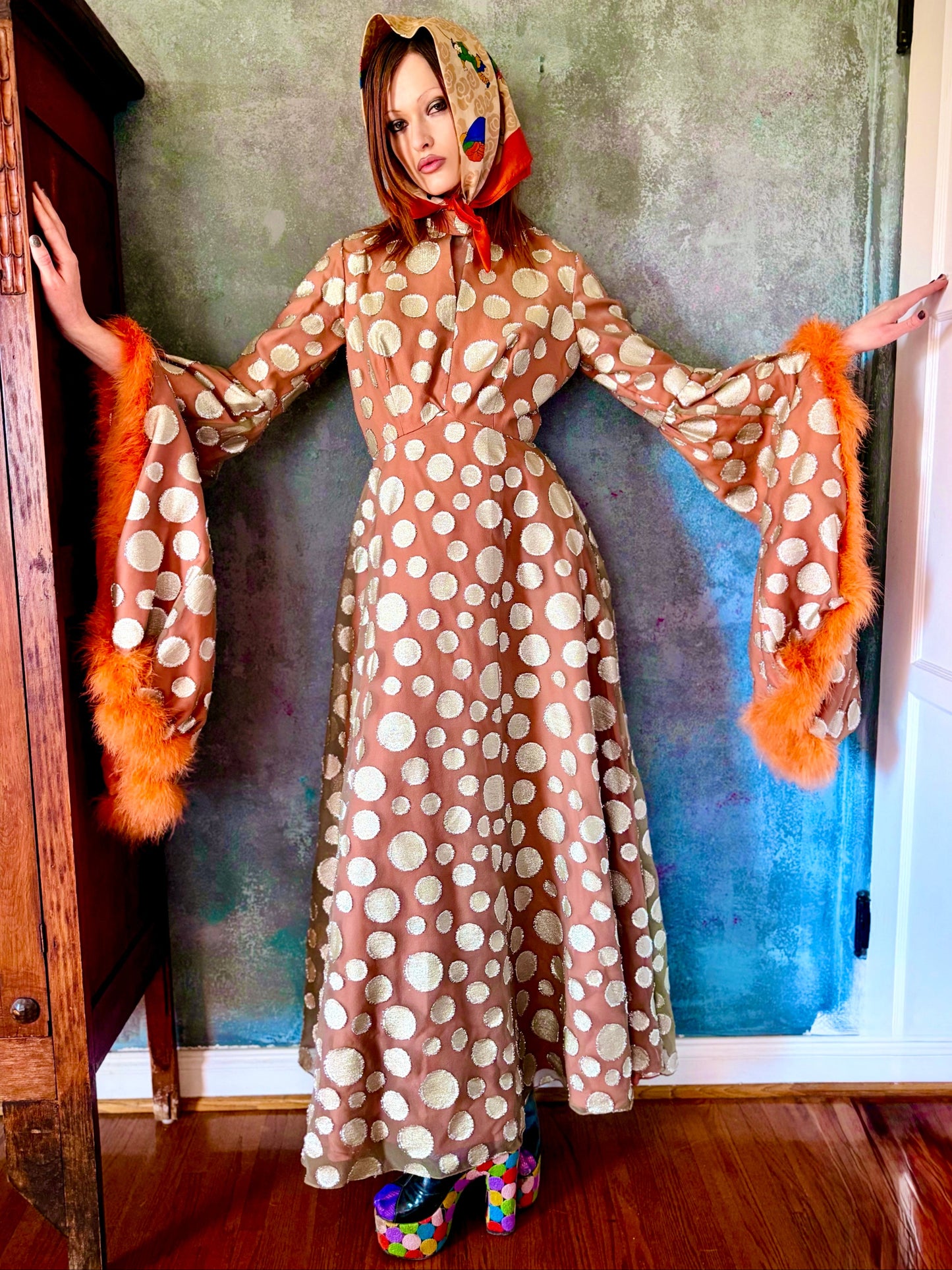 Woman in a vintage 1970s disco glamorous maxi dress with polka dots and orange accents standing outdoors.