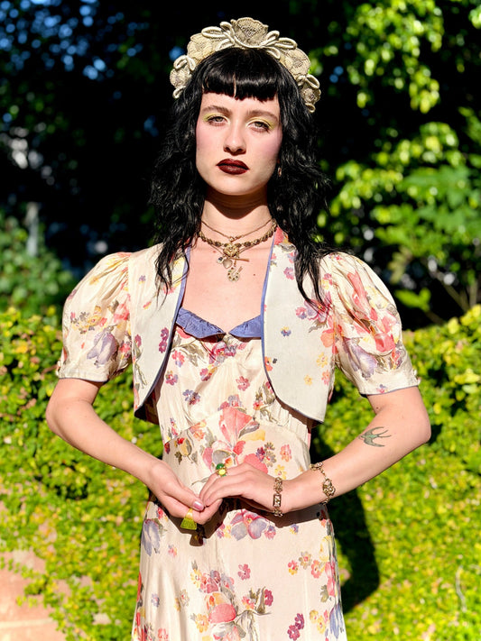 Woman in an antique 1930's floral dress with a headpiece standing outdoors with greenery in the background