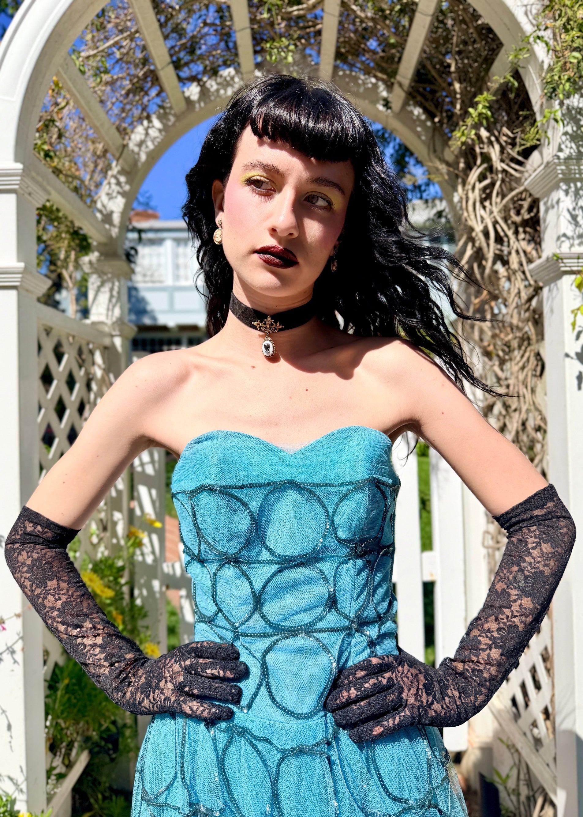 Woman in a 1950's blue strapless ball gown with black gloves standing in a garden.