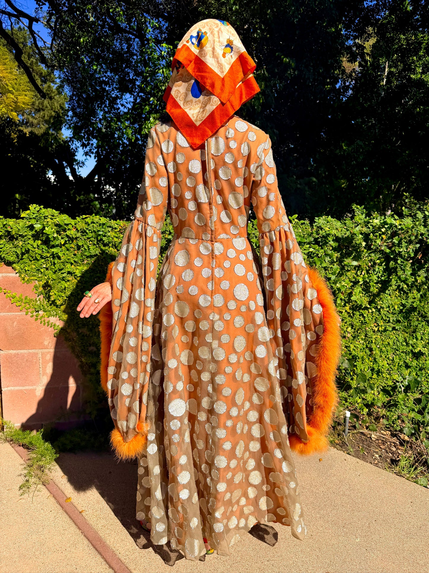 Woman in a vintage 1970s disco glamorous maxi dress with polka dots and orange accents standing outdoors.