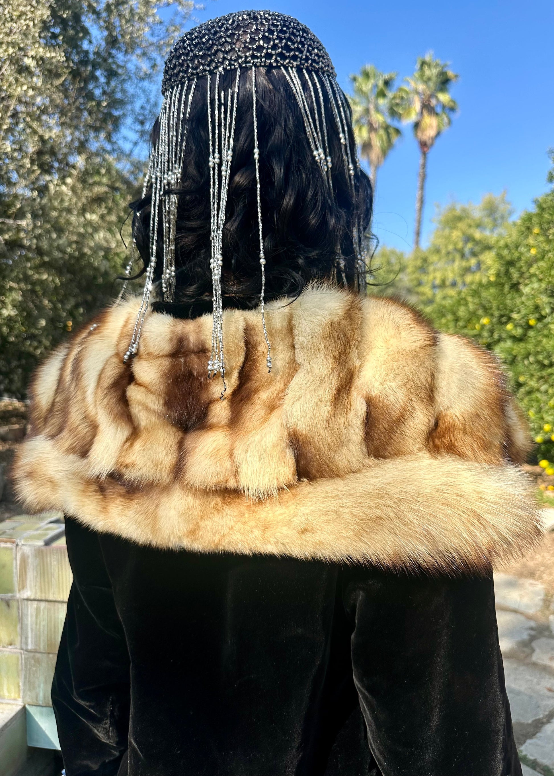 Person wearing an antique 1930's black fur-trimmed coat with a decorative headpiece outdoors.