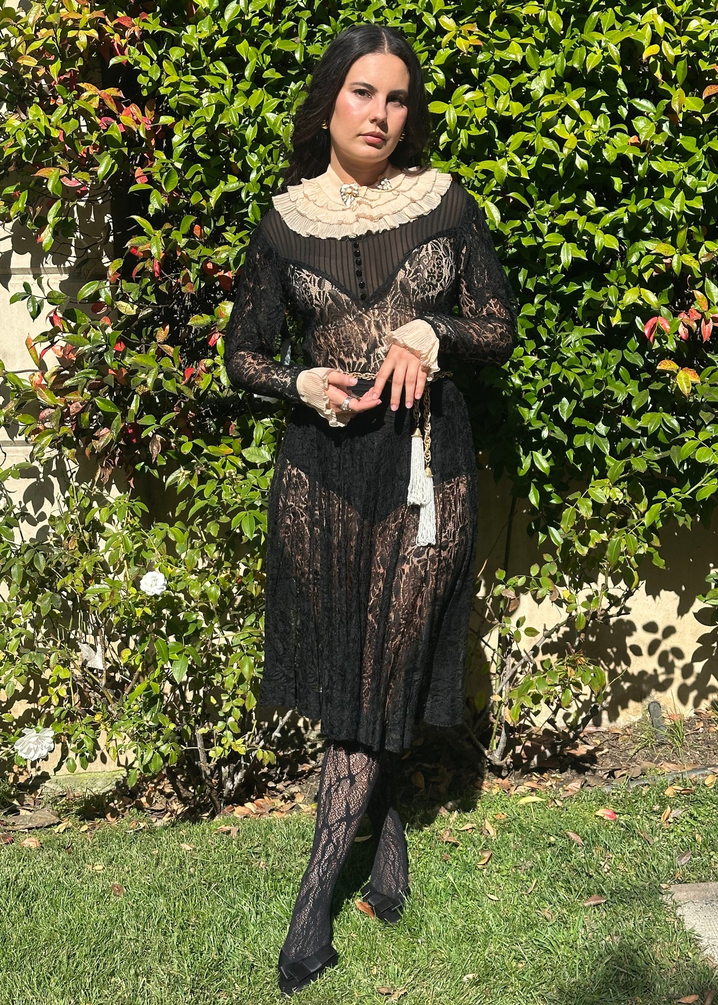 Person wearing a detailed black antique 1920's art deco dress with lace and embroidery, standing in front of an ornate metal gate.
