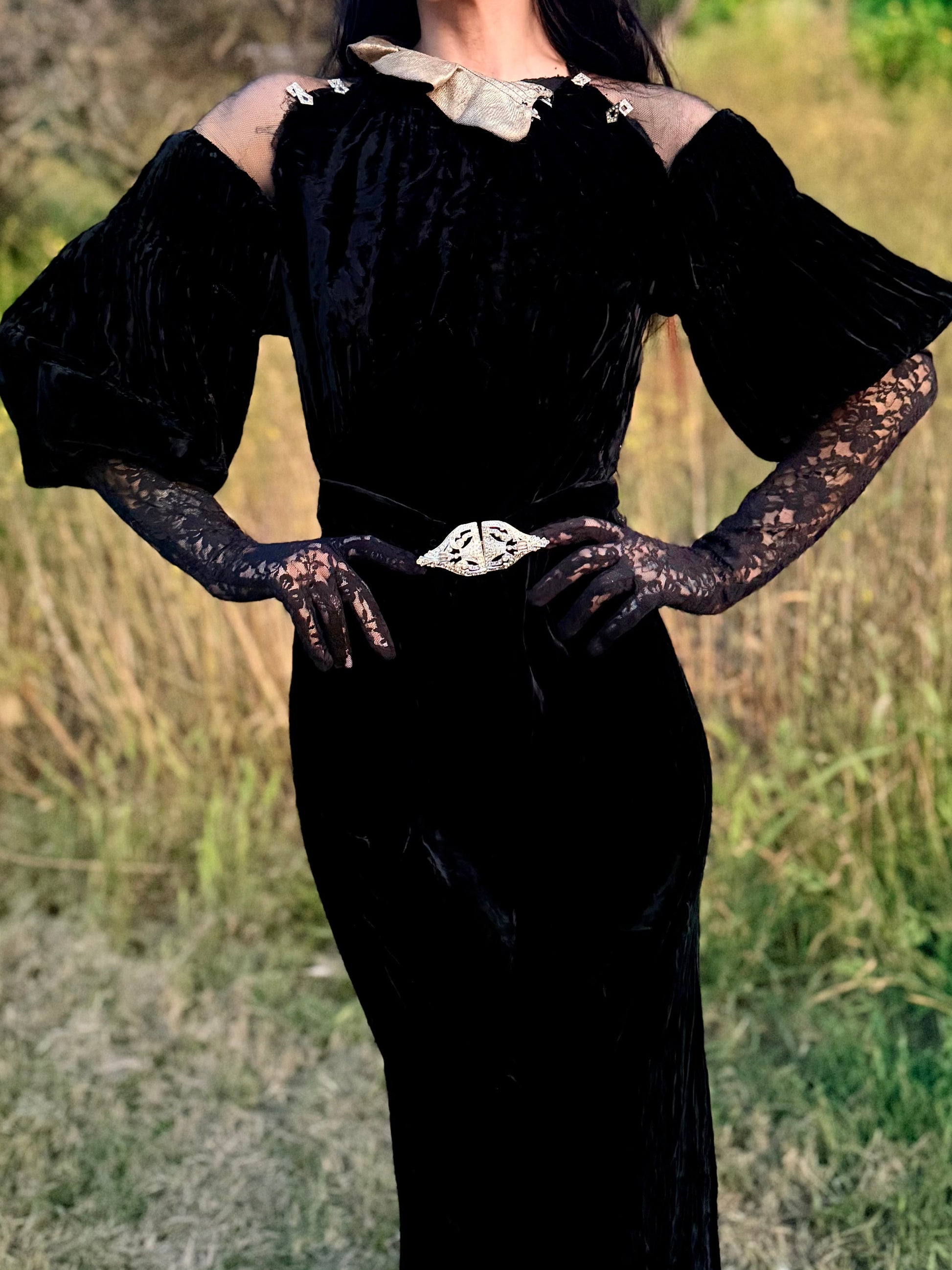 Woman wears antique 1930's black silk velvet Art Deco evening gown in field