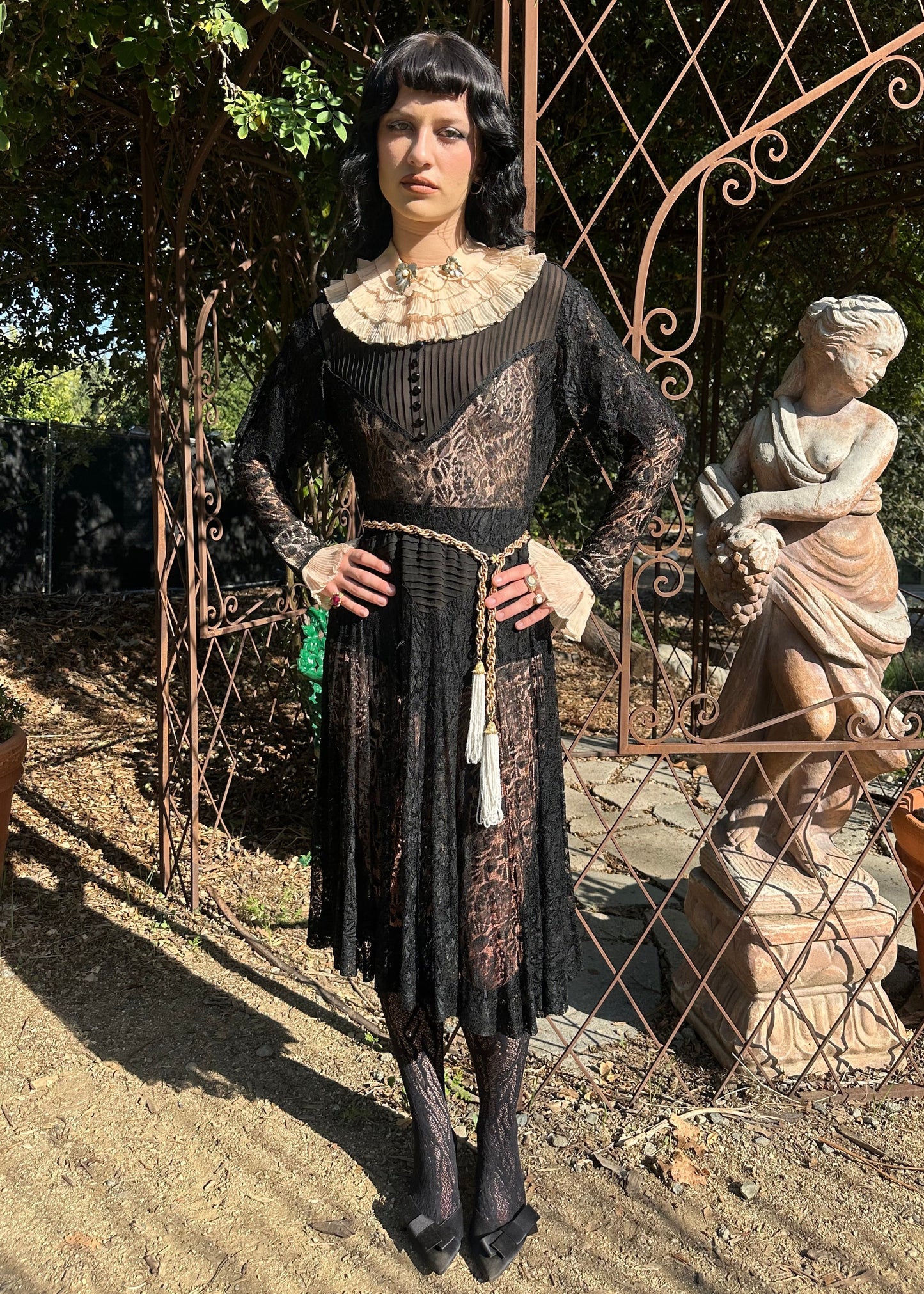 Person in an antique 1920s art deco vintage lace dress standing next to a statue in an outdoor setting