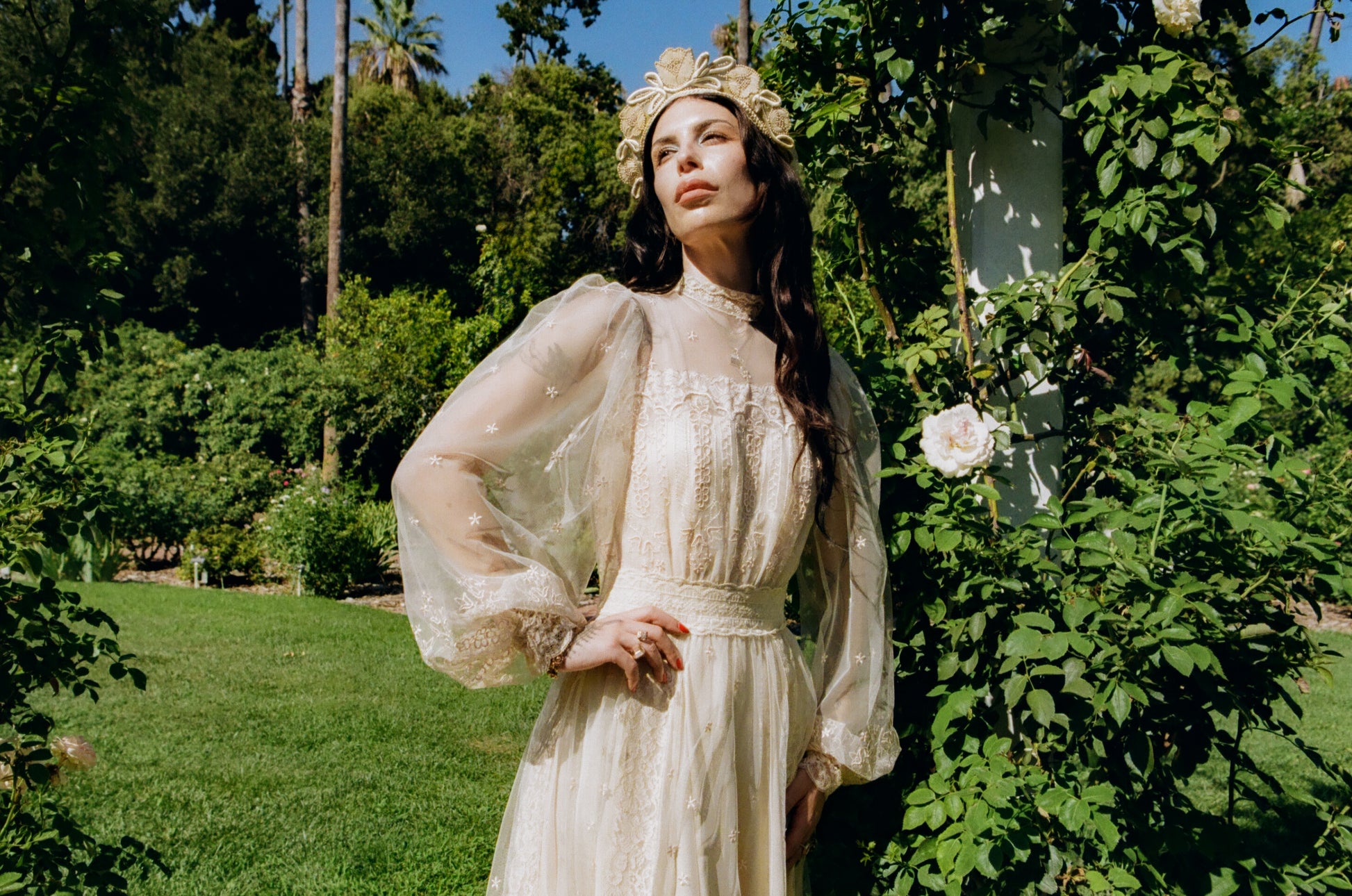 Woman in a white dress standing in a garden with greenery and flowers.