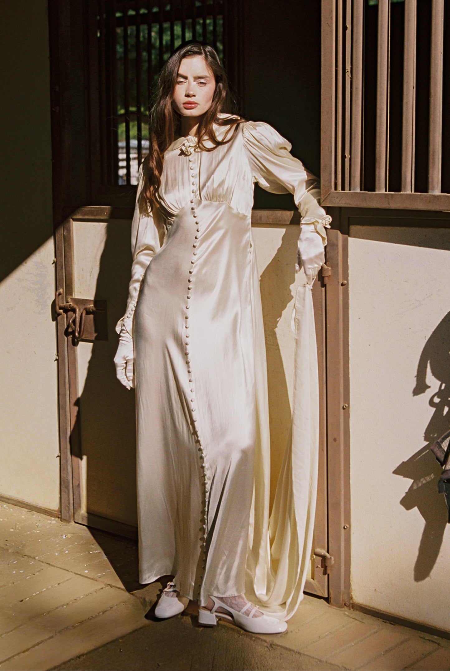 Woman in a long, light-colored dress standing in a traditional setting.