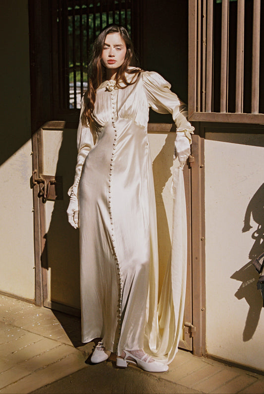 Woman in a long, light-colored dress standing in a traditional setting.