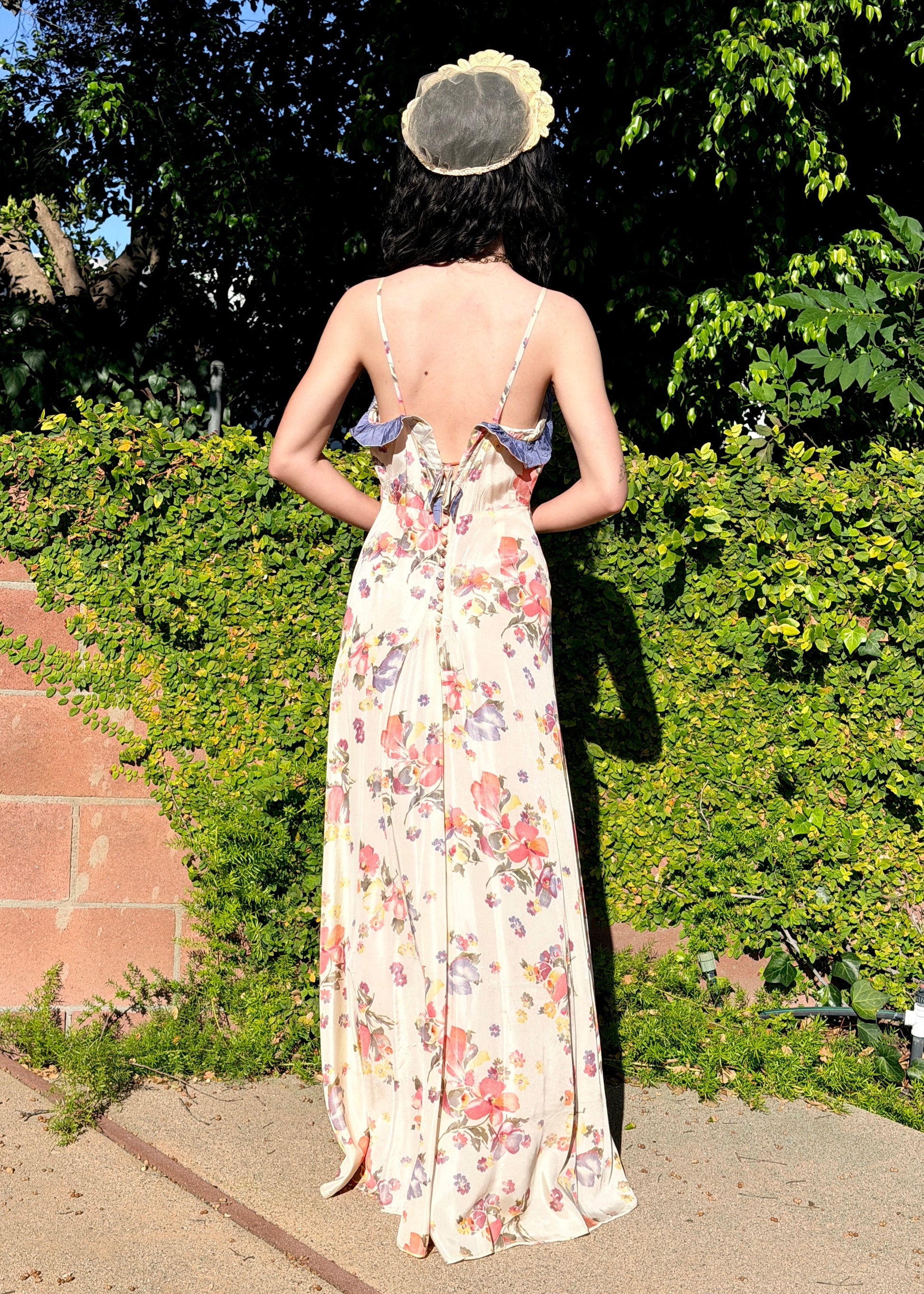 Woman in a floral  antique 1930s floral dress standing outdoors with greenery in the background