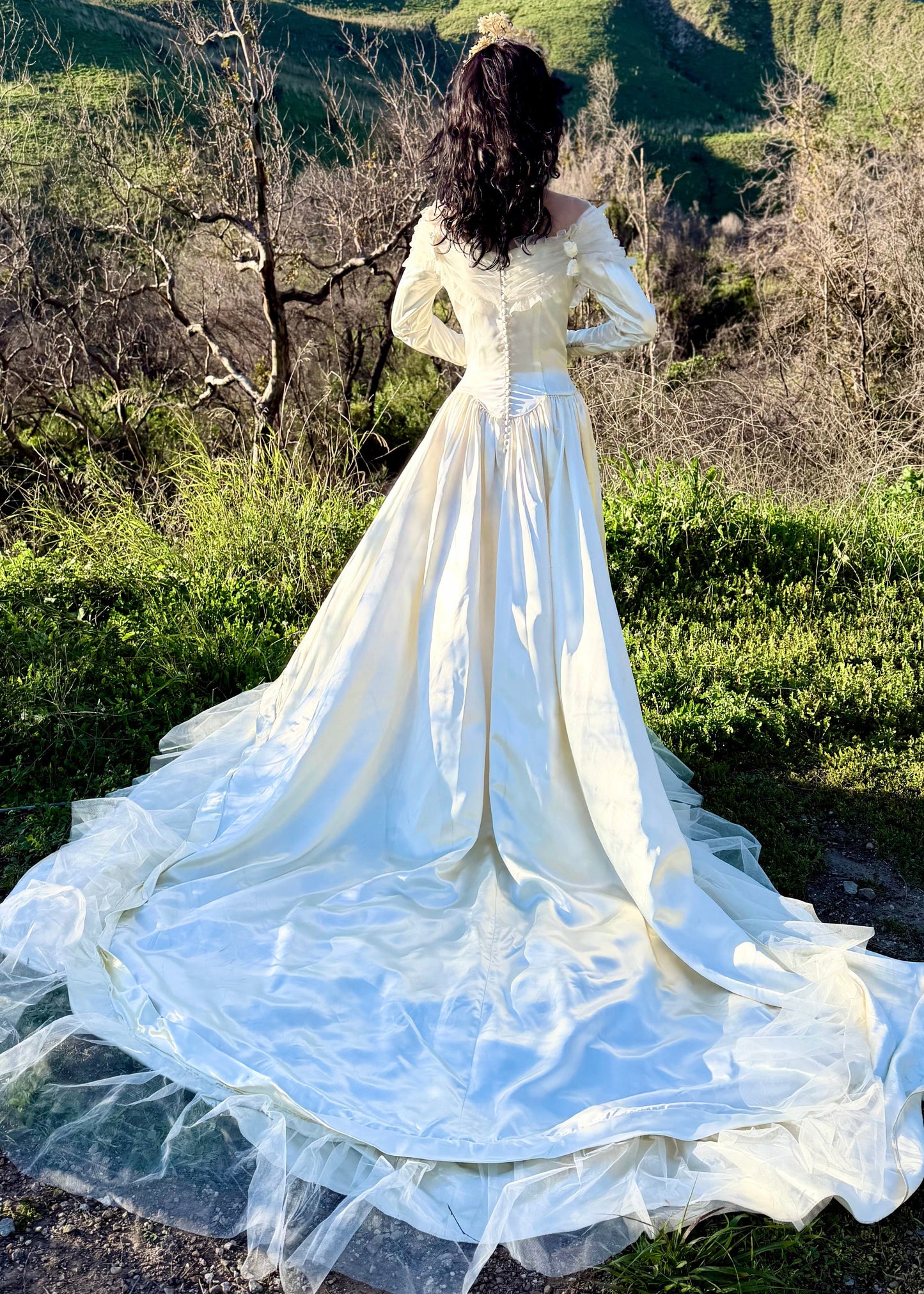 Woman in a white dress standing in a natural landscape with green hills and trees.