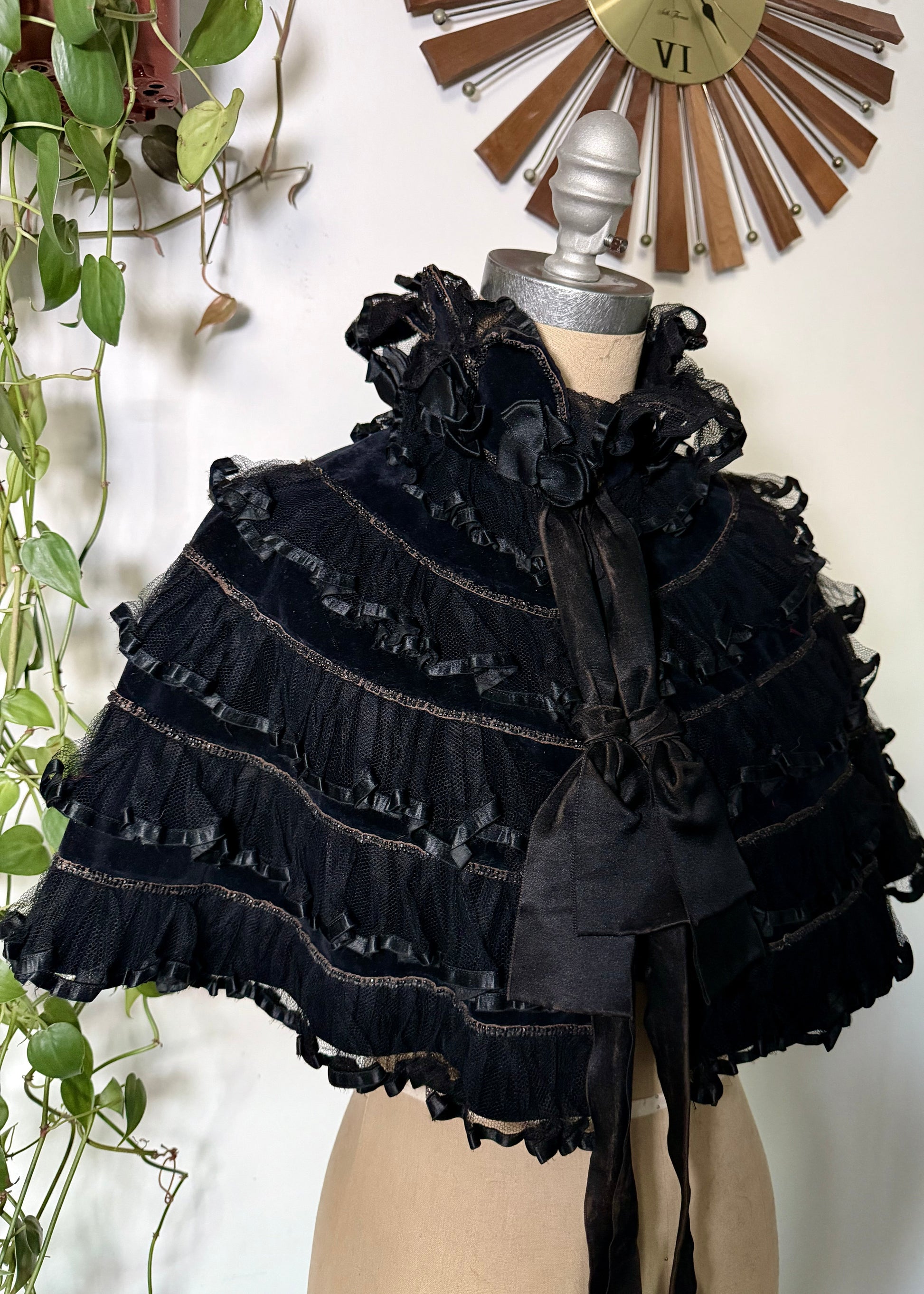Black ruffled garment on a mannequin against a white wall with decorative elements.