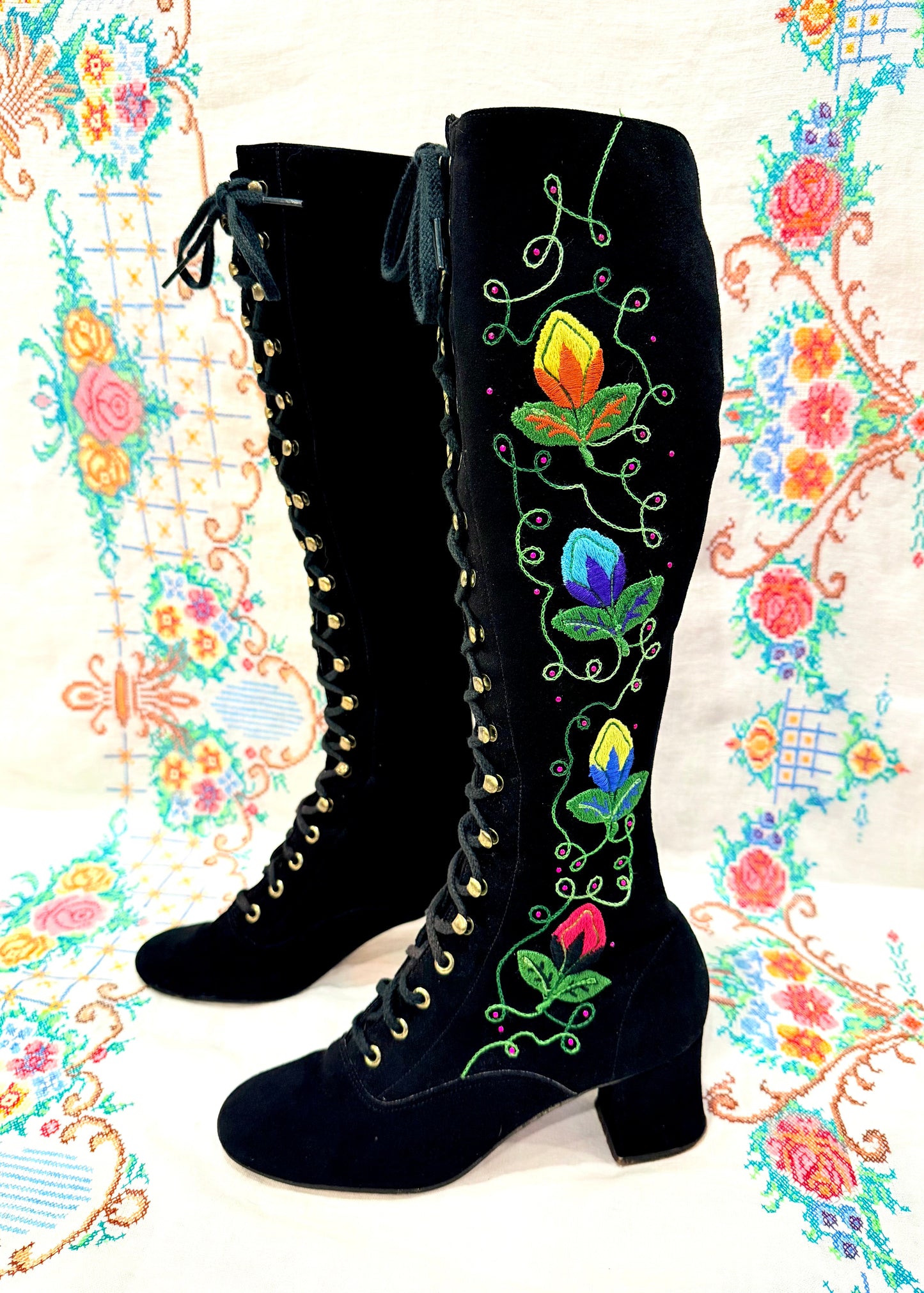 Black knee-high 1960's suede penny lane gogo boots with colorful floral embroidery on a decorative background