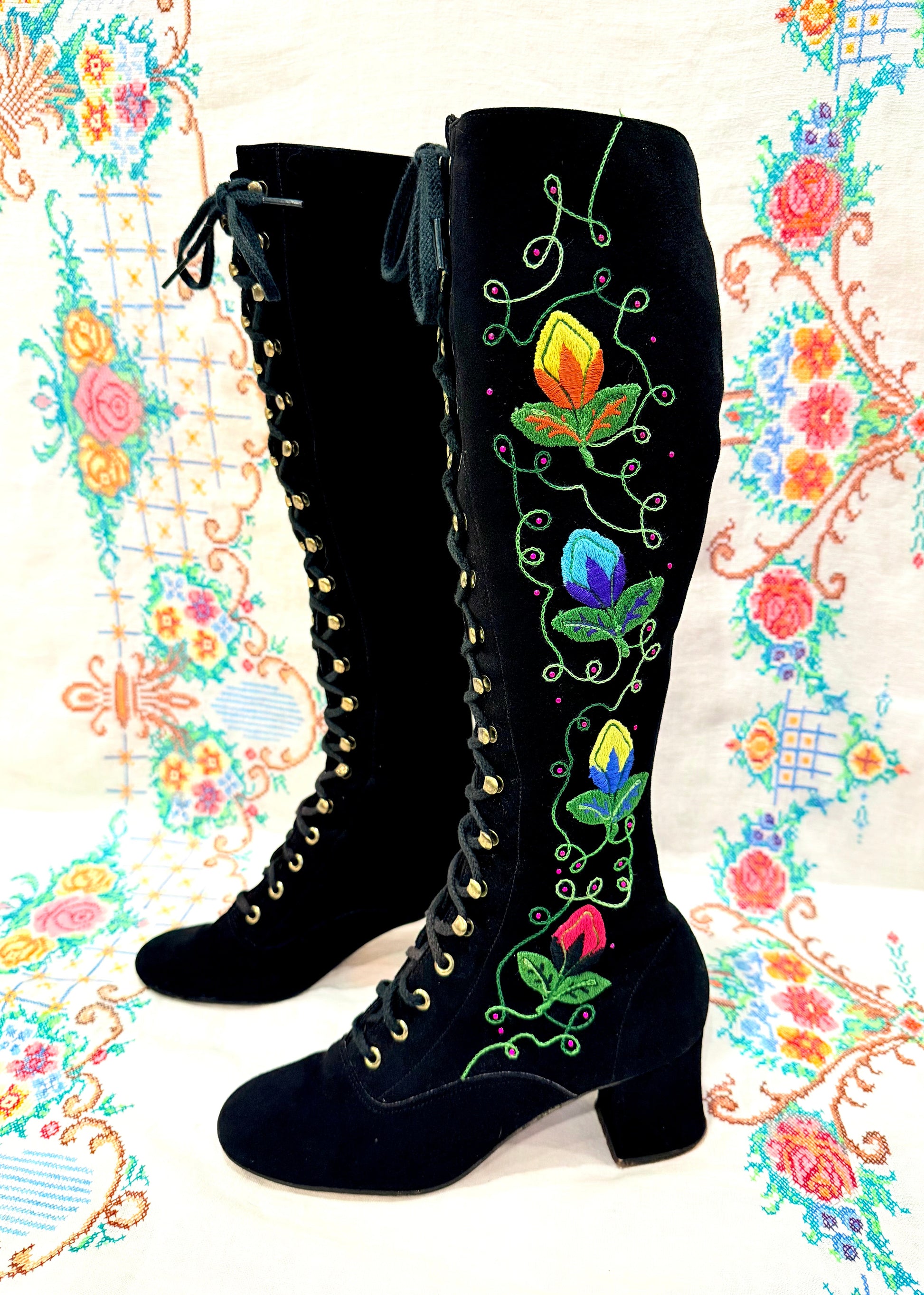 Black knee-high 1960's suede penny lane gogo boots with colorful floral embroidery on a decorative background