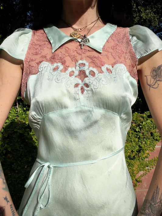 Woman in an antique 1930's silk slip in mint green with a floral headpiece against a wall with framed paintings.