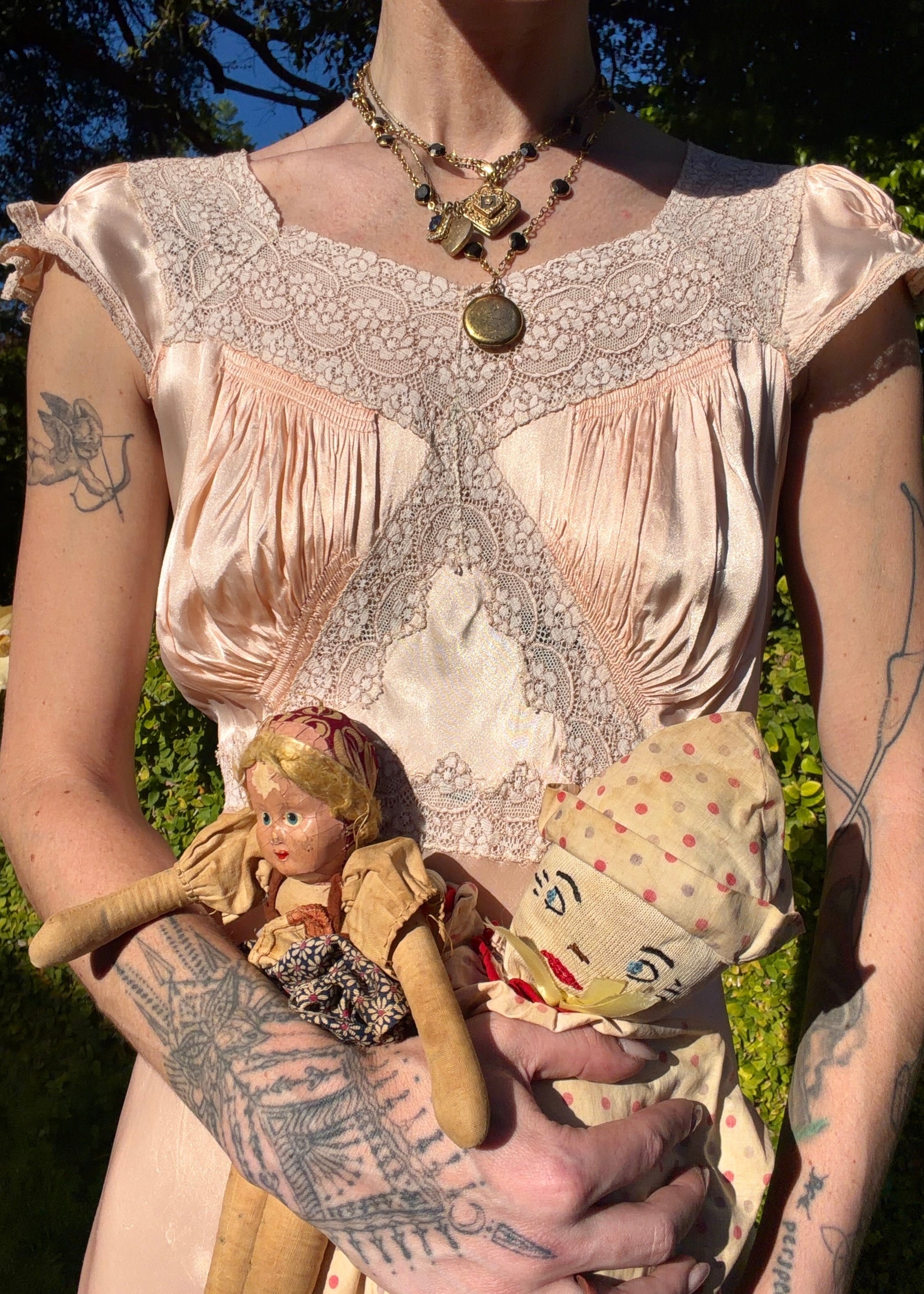 Woman wearing a long bias cut, elegant antique 1930's silk slip dress in a light pink color in an outdoor setting.