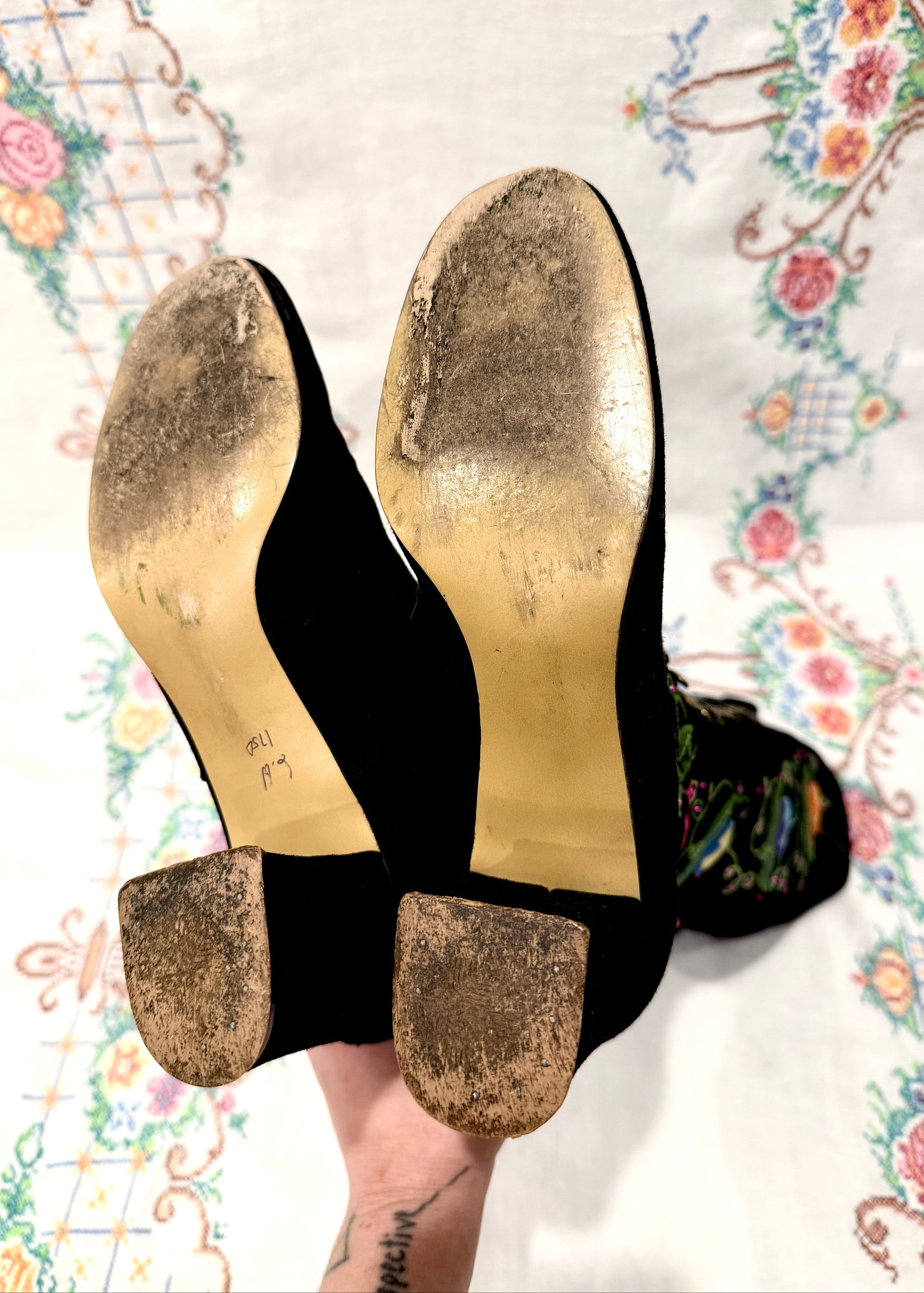 Black knee-high vintage 1960's suede penny lane gogo boots with colorful floral embroidery on a decorative background