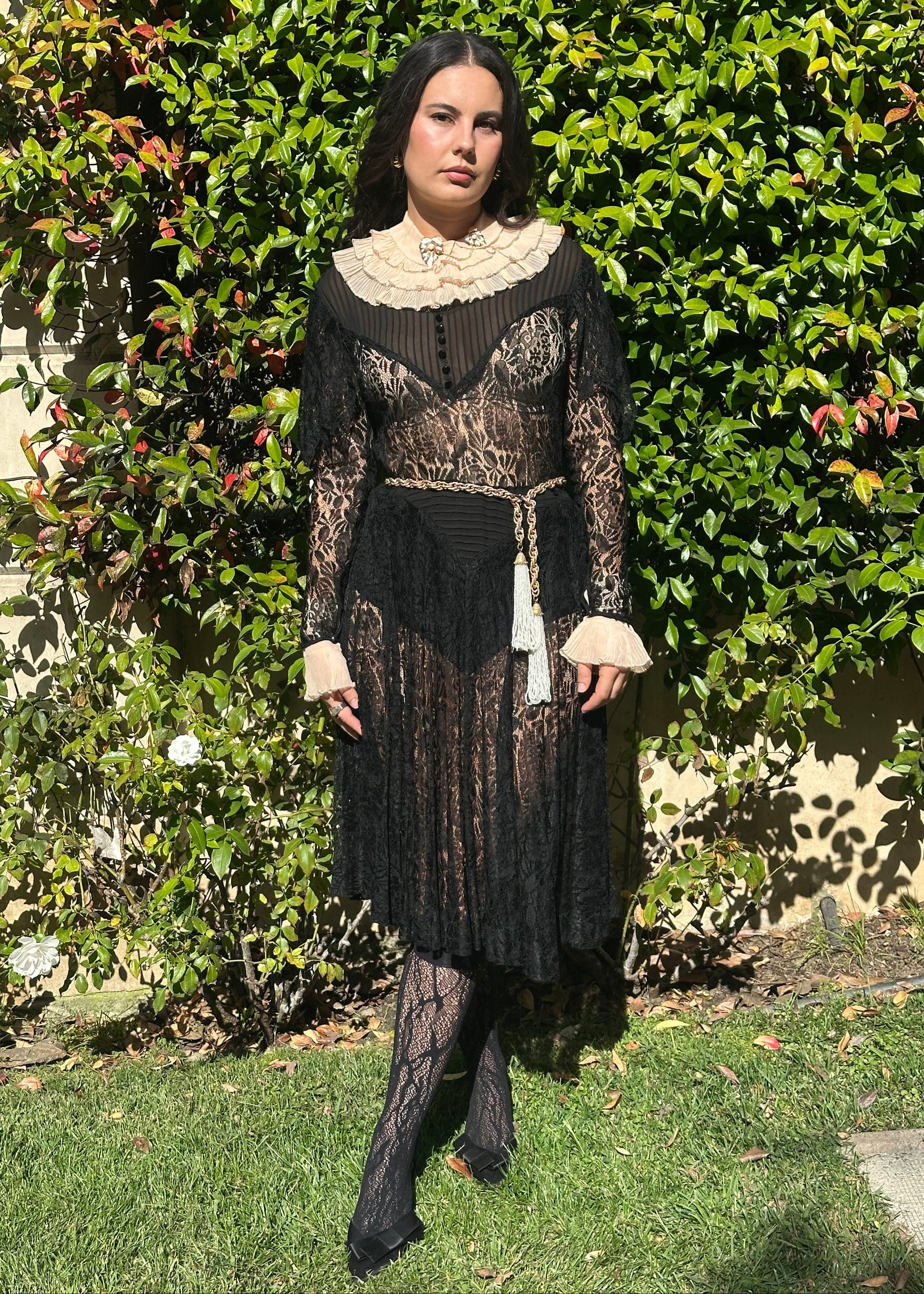Person wearing a detailed black antique 1920's art deco dress with lace and embroidery, standing in front of an ornate metal gate.