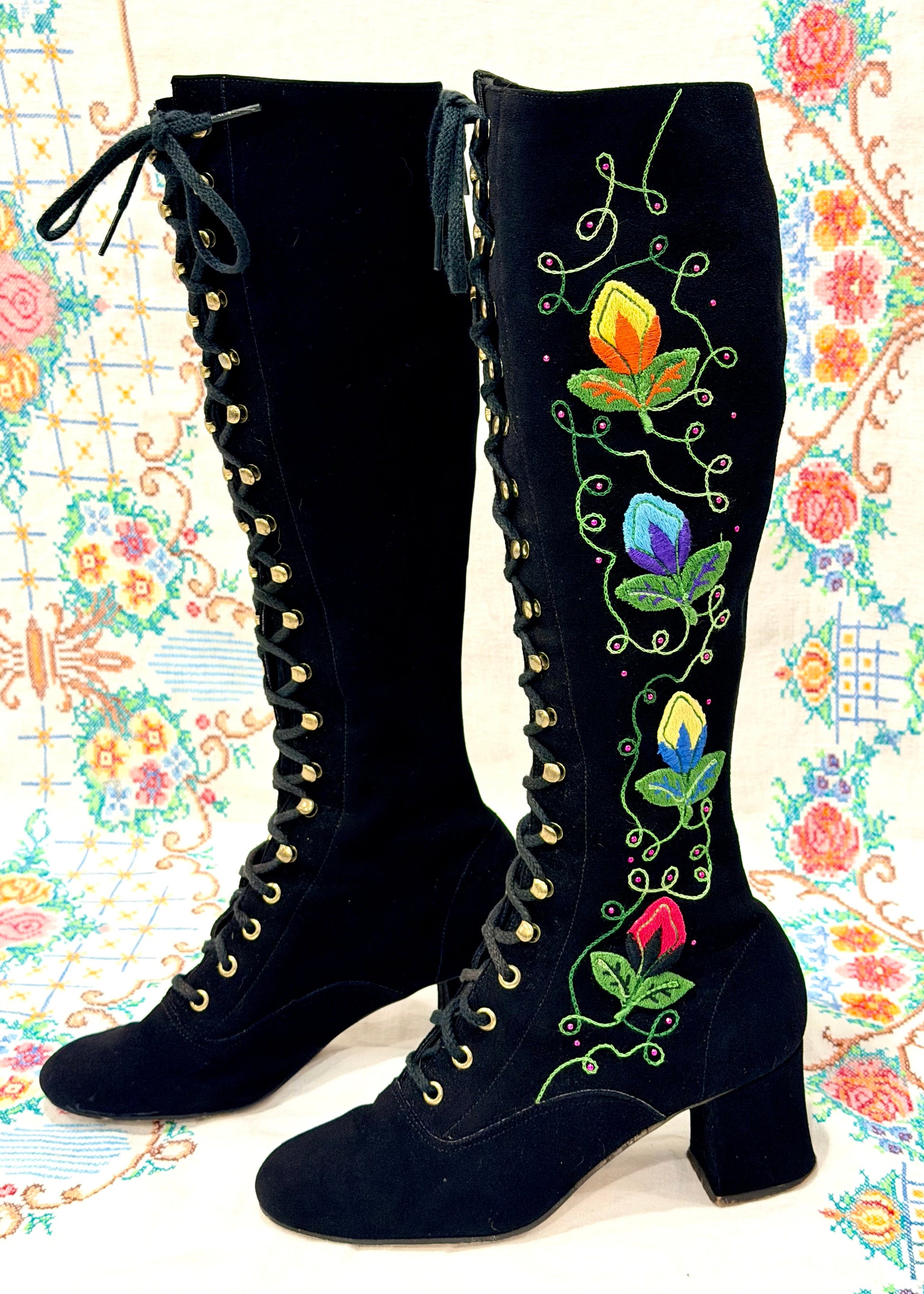 Black knee-high vintage 1960's suede penny lane gogo boots with colorful floral embroidery on a decorative background