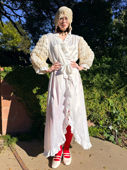 Person wearing a white dress with red shoes standing outdoors with trees in the background