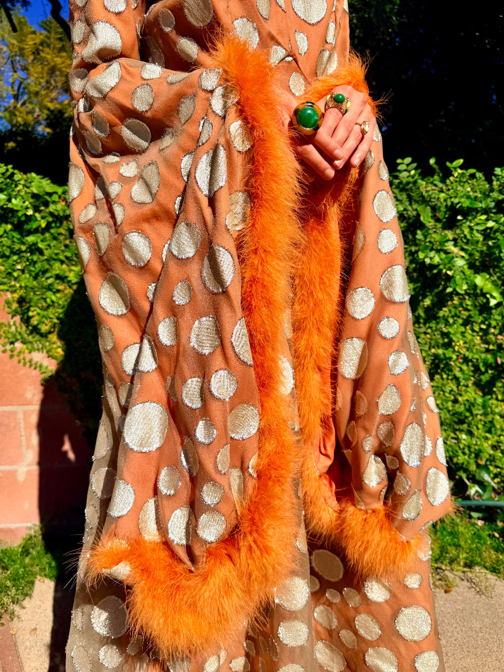 Woman in a vintage 1970's chiffon polka dot maxi dress with marabou feather accents standing outdoors.