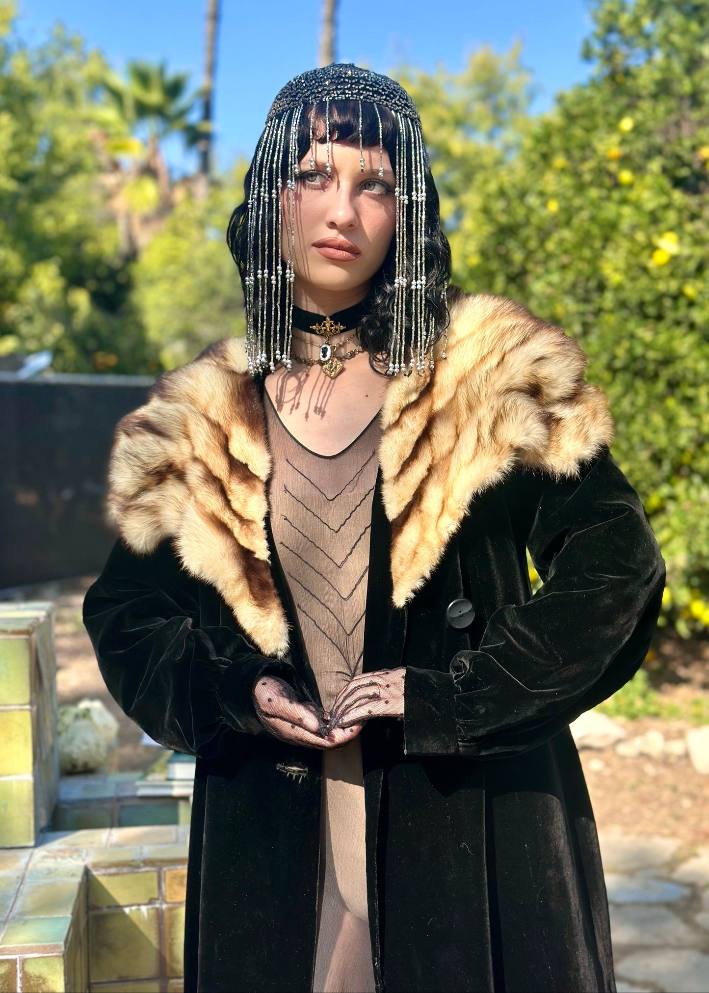 Person wearing a black coat with fur collar and a decorative headpiece outdoors.