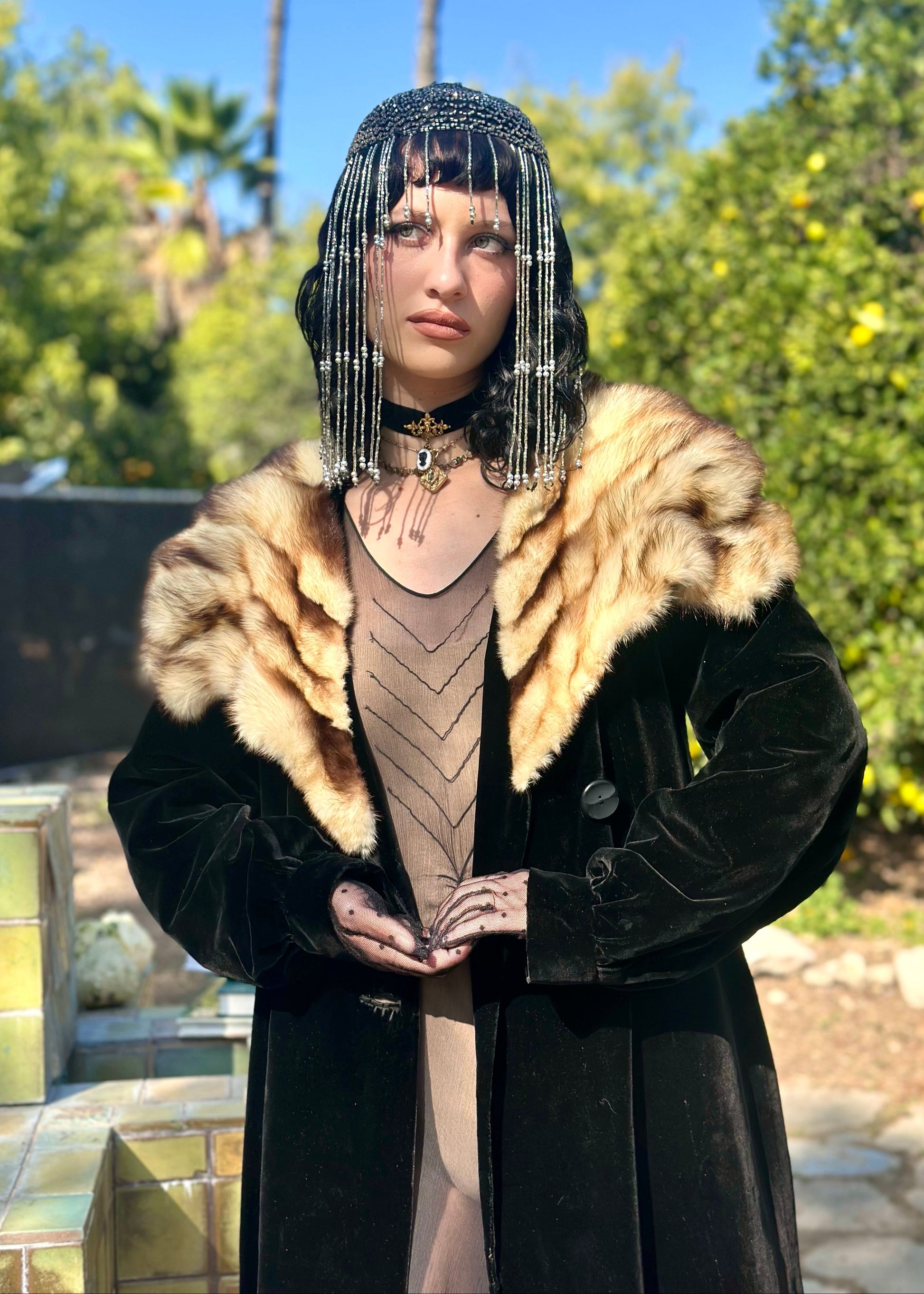 Person wearing a black coat with fur collar and a decorative headpiece outdoors.