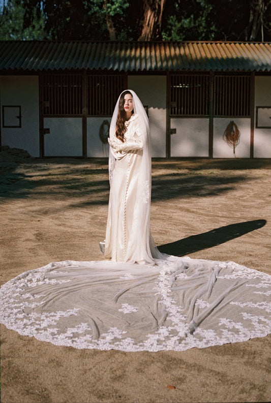 Woman in a white wedding dress with a long train standing outdoors.