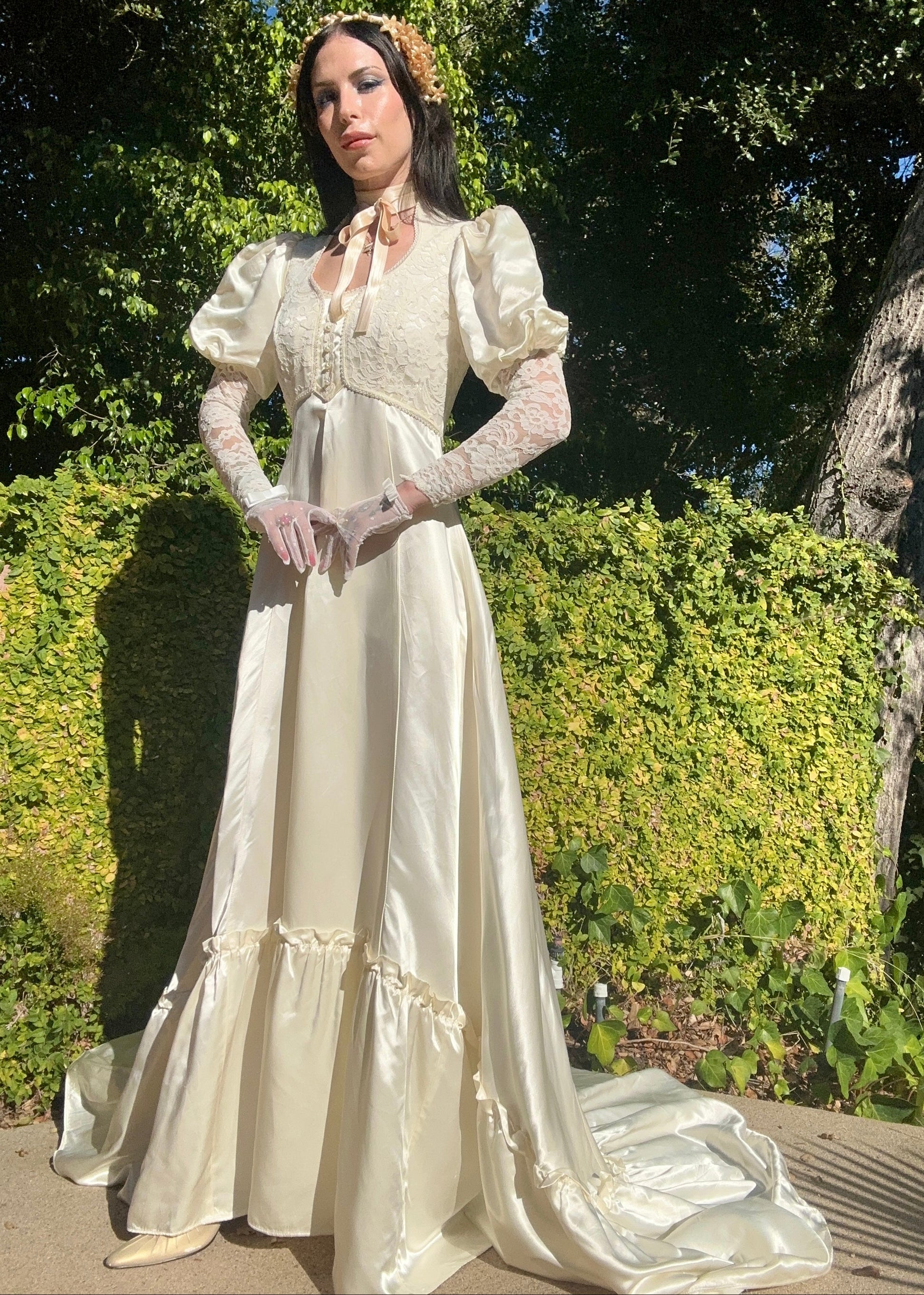 Woman in a vintage-style white dress standing outdoors with greenery in the background