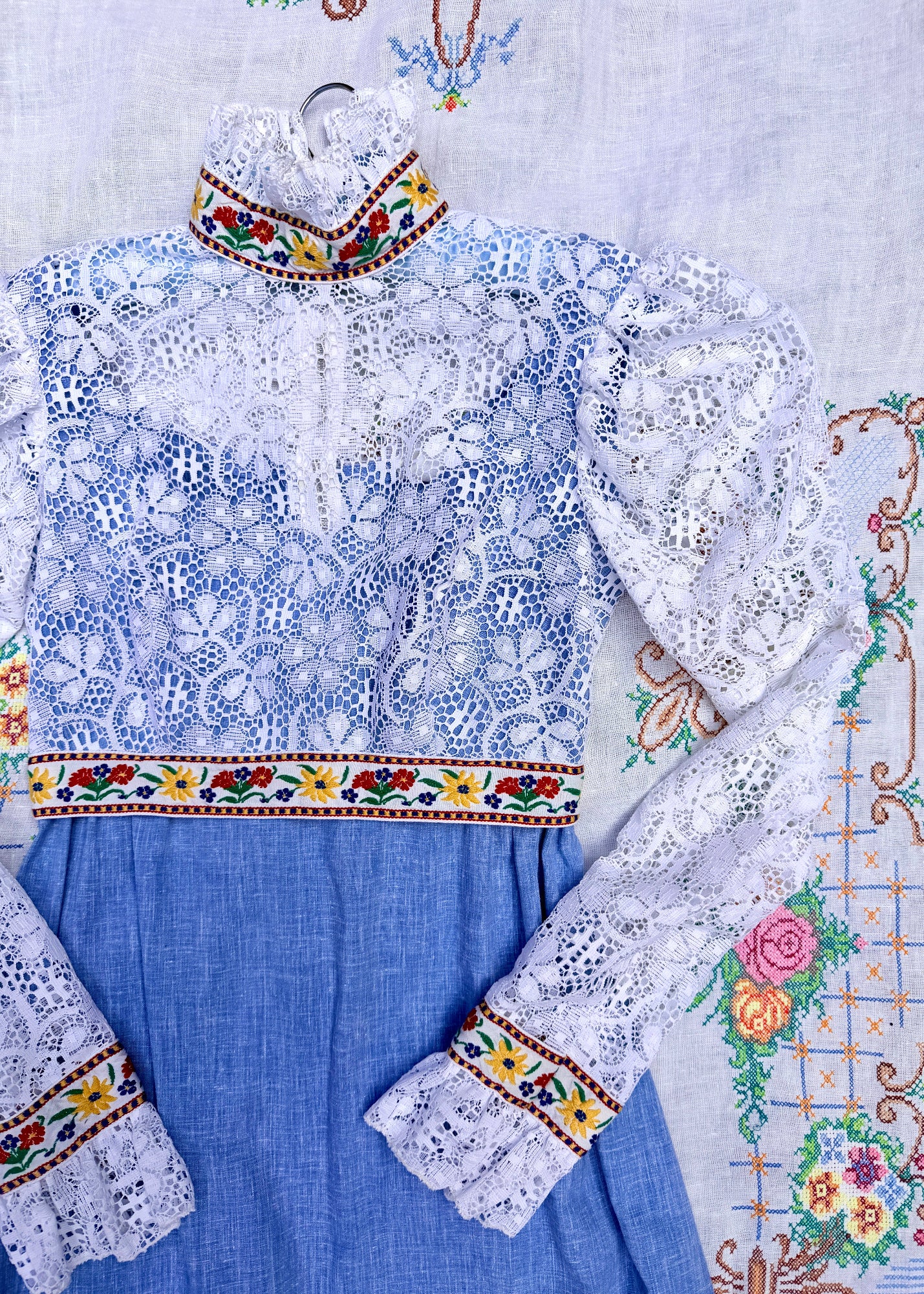 A traditional Ukrainian embroidered blouse and skirt set in blue and white, featuring intricate lace embroidery, floral patterns, and colorful embroidered borders on the collar, waist, and cuffs.