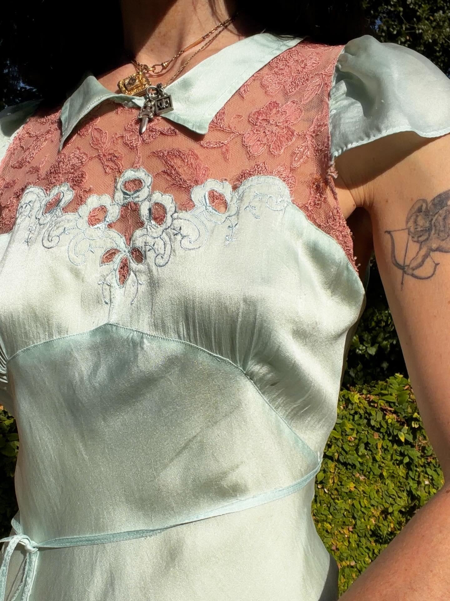 Woman in an antique 1930's silk slip in mint green with a floral headpiece against a wall with framed paintings.