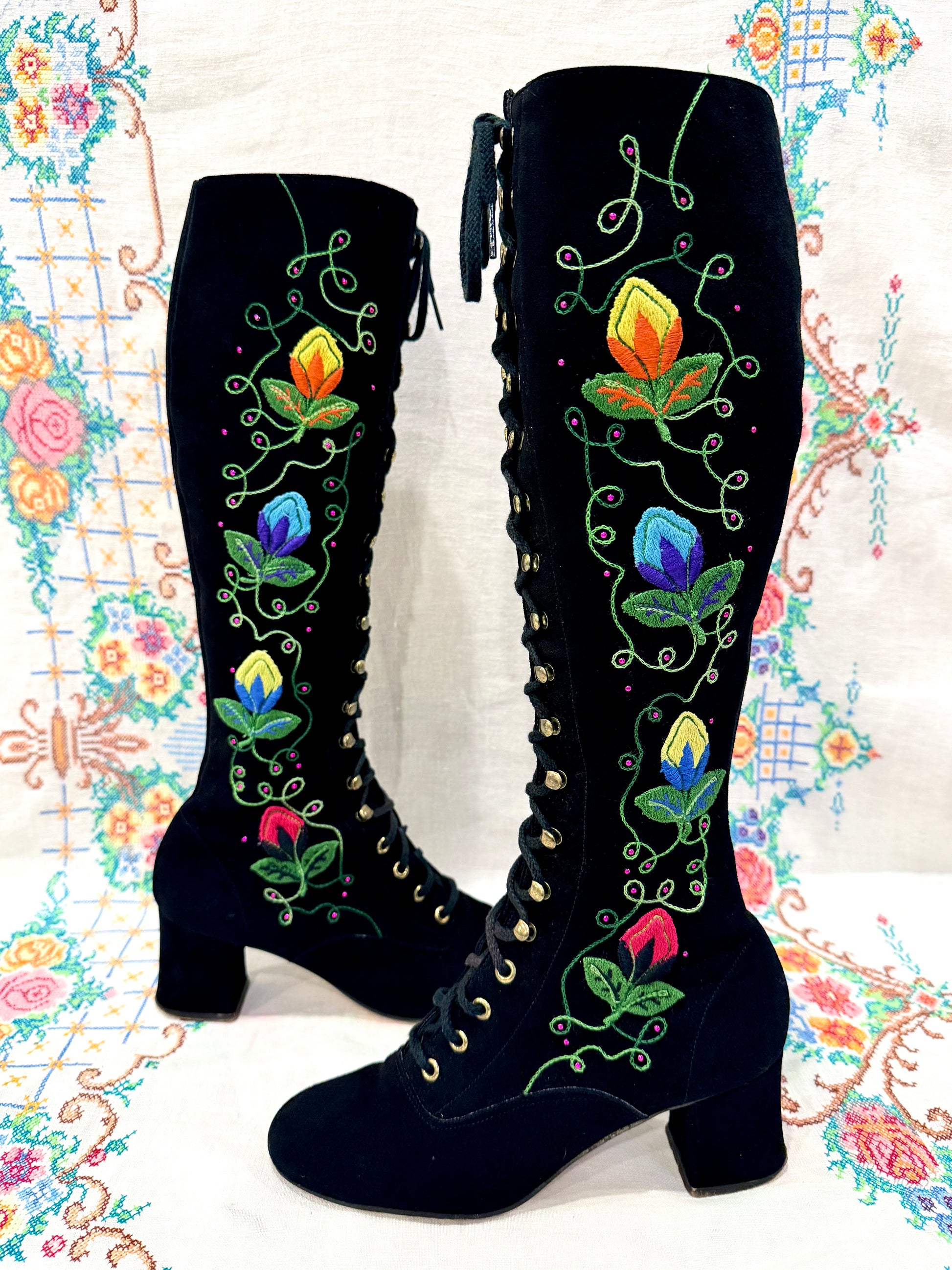 Black knee-high 1960's suede penny lane gogo boots with colorful floral embroidery on a decorative background