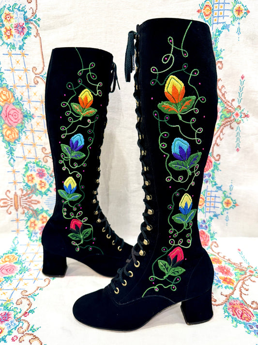 Black knee-high 1960's suede penny lane gogo boots with colorful floral embroidery on a decorative background