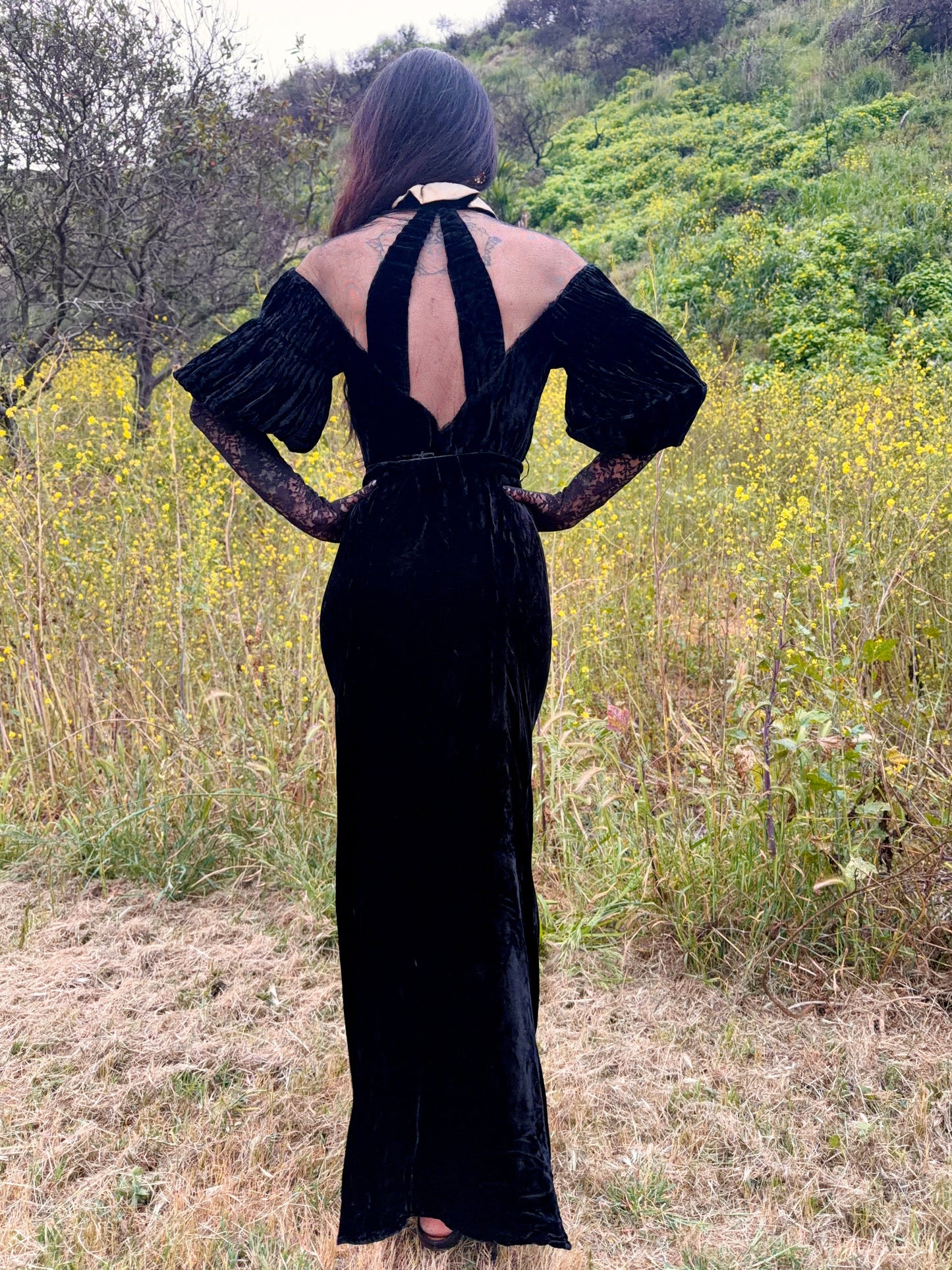 Woman wears antique 1930's black silk velvet Art Deco evening gown in field
