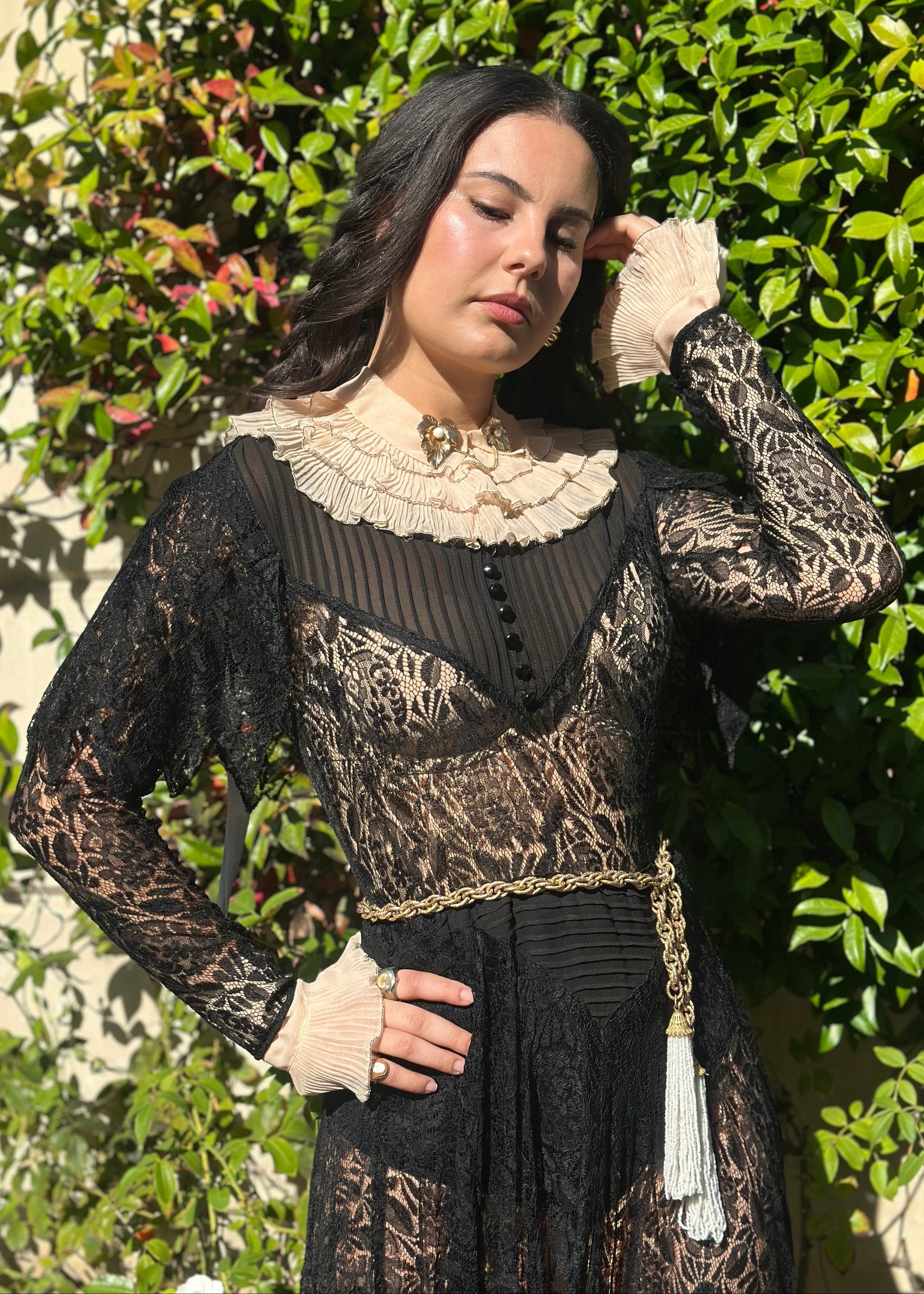 Person wearing a detailed black antique 1920's art deco dress with lace and embroidery, standing in front of an ornate metal gate.