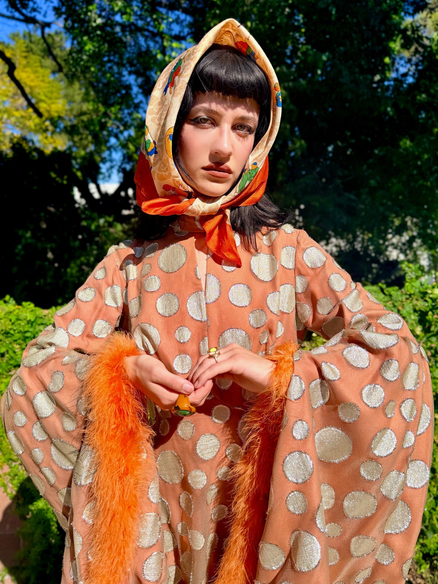 Woman in a vintage 1970s disco glamorous maxi dress with polka dots and orange accents standing outdoors.