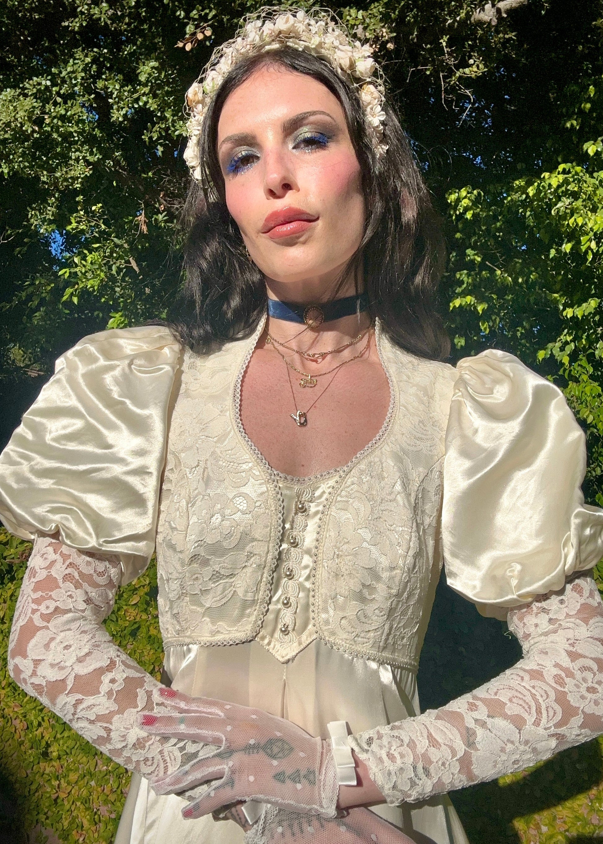 Woman in a Gunnee Sax wedding dress with lace sleeves and a floral headpiece, standing outdoors.