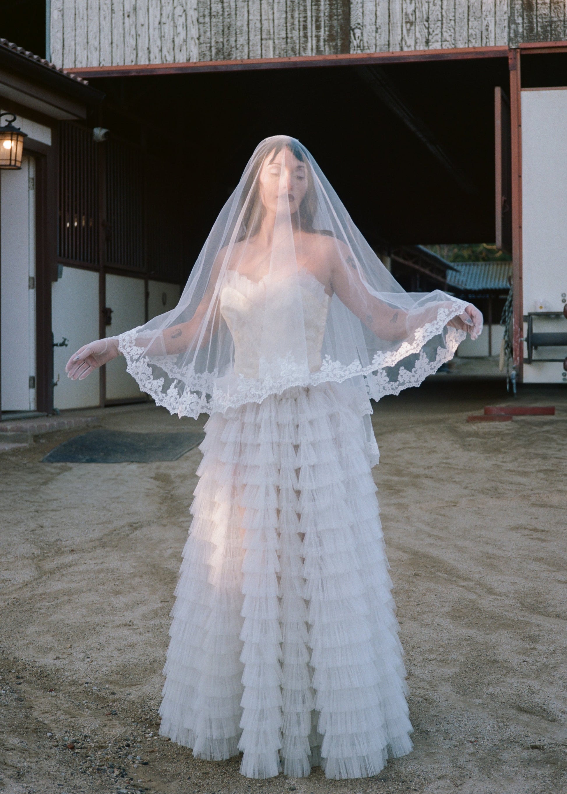 Woman in a vintage wedding dress with a veil standing in front of a rustic building.