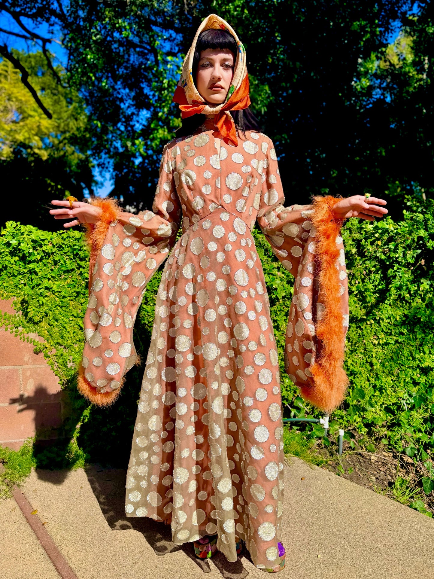 Woman in a vintage 1970s disco glamorous maxi dress with polka dots and orange accents standing outdoors.